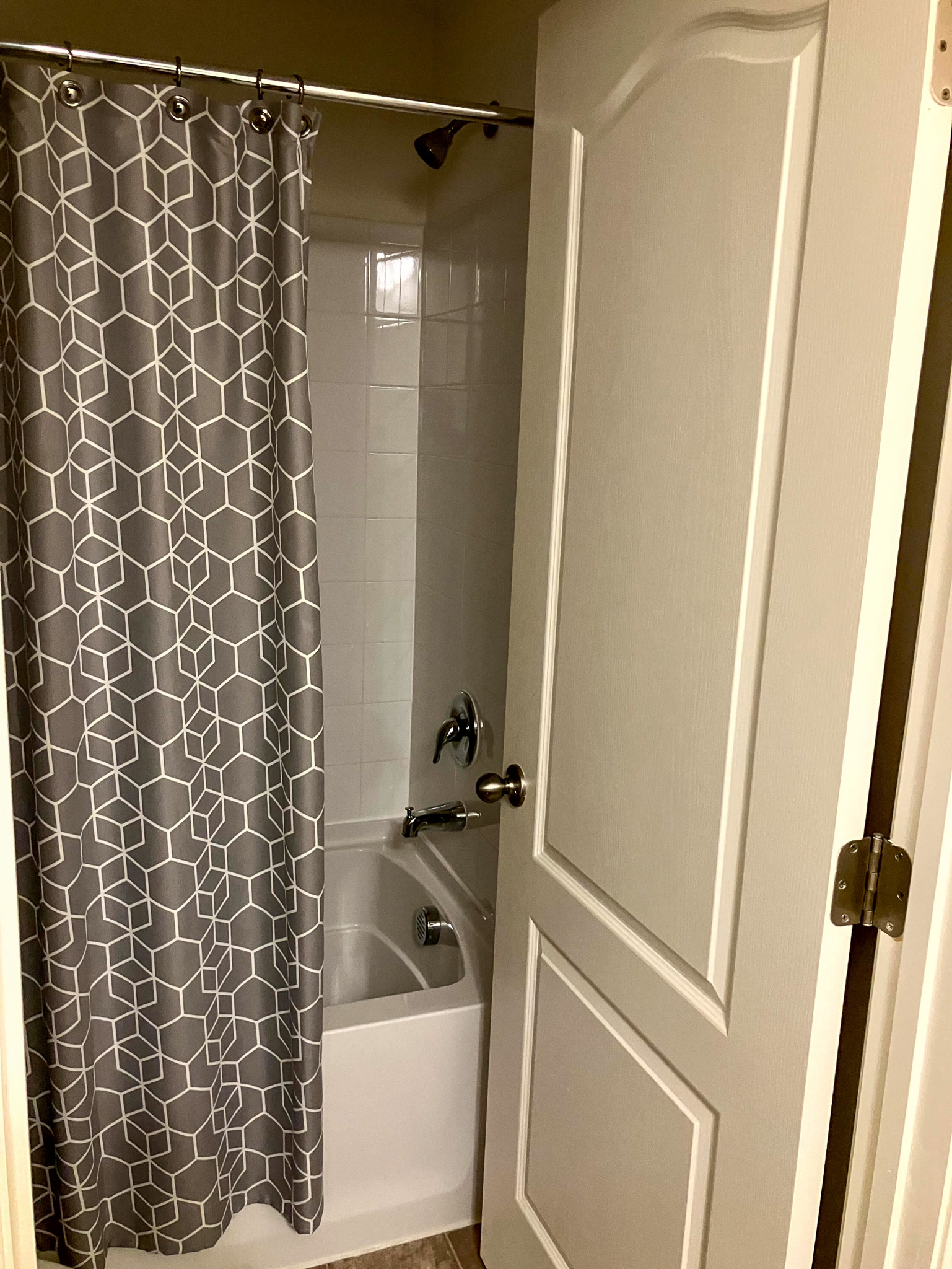 A bathroom with a white bathtub and shower behind a gray patterned curtain, viewed through an open door inside the home of Torwon and Deljuan Mitchell in Fredericksburg, Virginia.