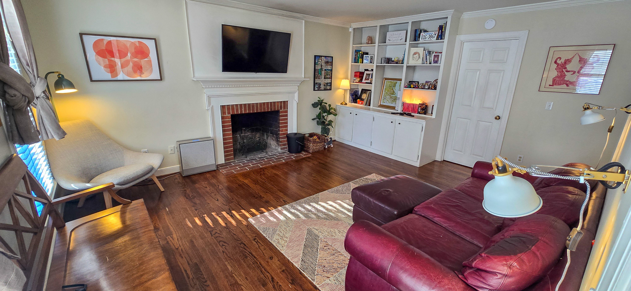 Living room with a brick fireplace, wall‑mounted TV, built‑in shelves, red sofa, and wood flooring inside the home of Group Home Provider Jared Nepal in Fredericksburg, Virginia.