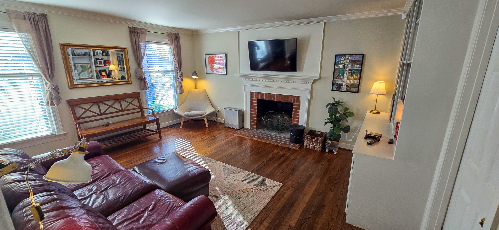 Bright living room with a leather sectional, wood floors, a fireplace with a TV above it, large windows, and framed art on the walls inside the home of Group Home Provider Jared Nepal in Fredericksburg, Virginia.
