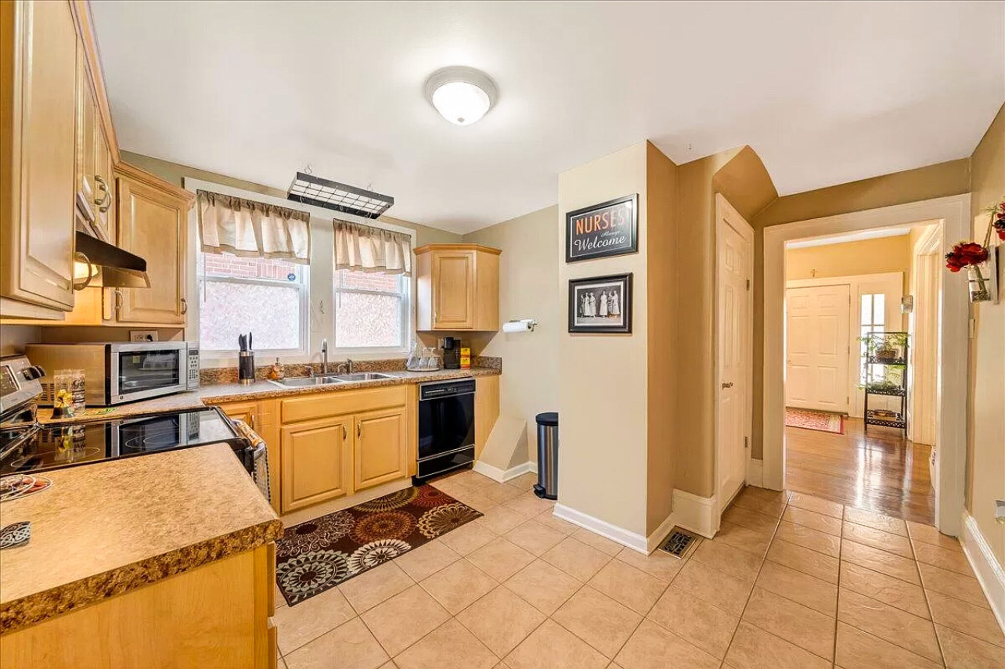 A kitchen with light wood cabinets, tiled floors, black appliances, and an open hallway leading to another room inside the home of Sponsored Residential Provider Jessica Peregrino in Roanoke, Virginia.