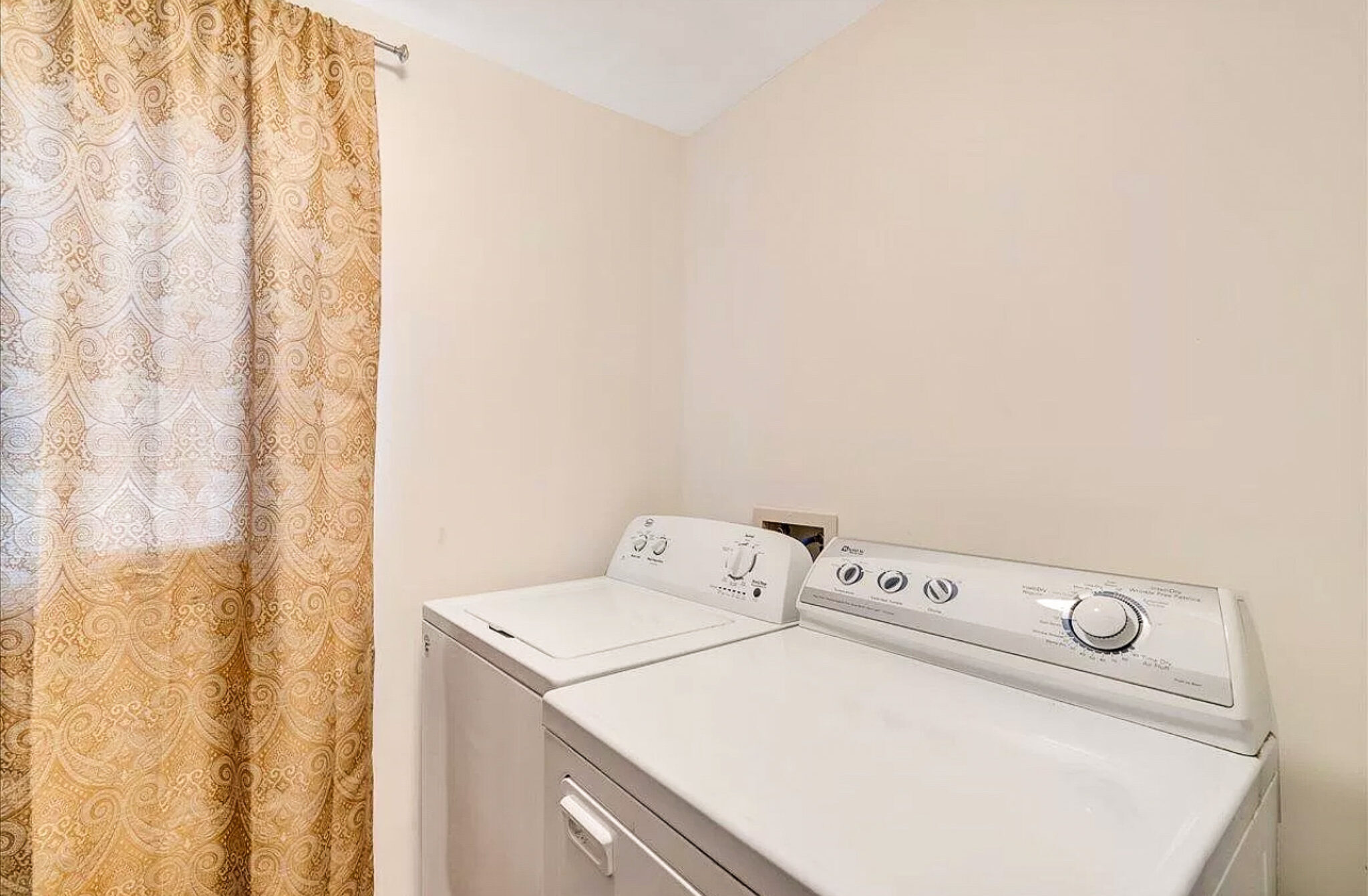 A laundry area with a washing machine and dryer beside a window with patterned curtains inside the home of Sponsored Residential Provider Jessica Peregrino in Roanoke, Virginia.