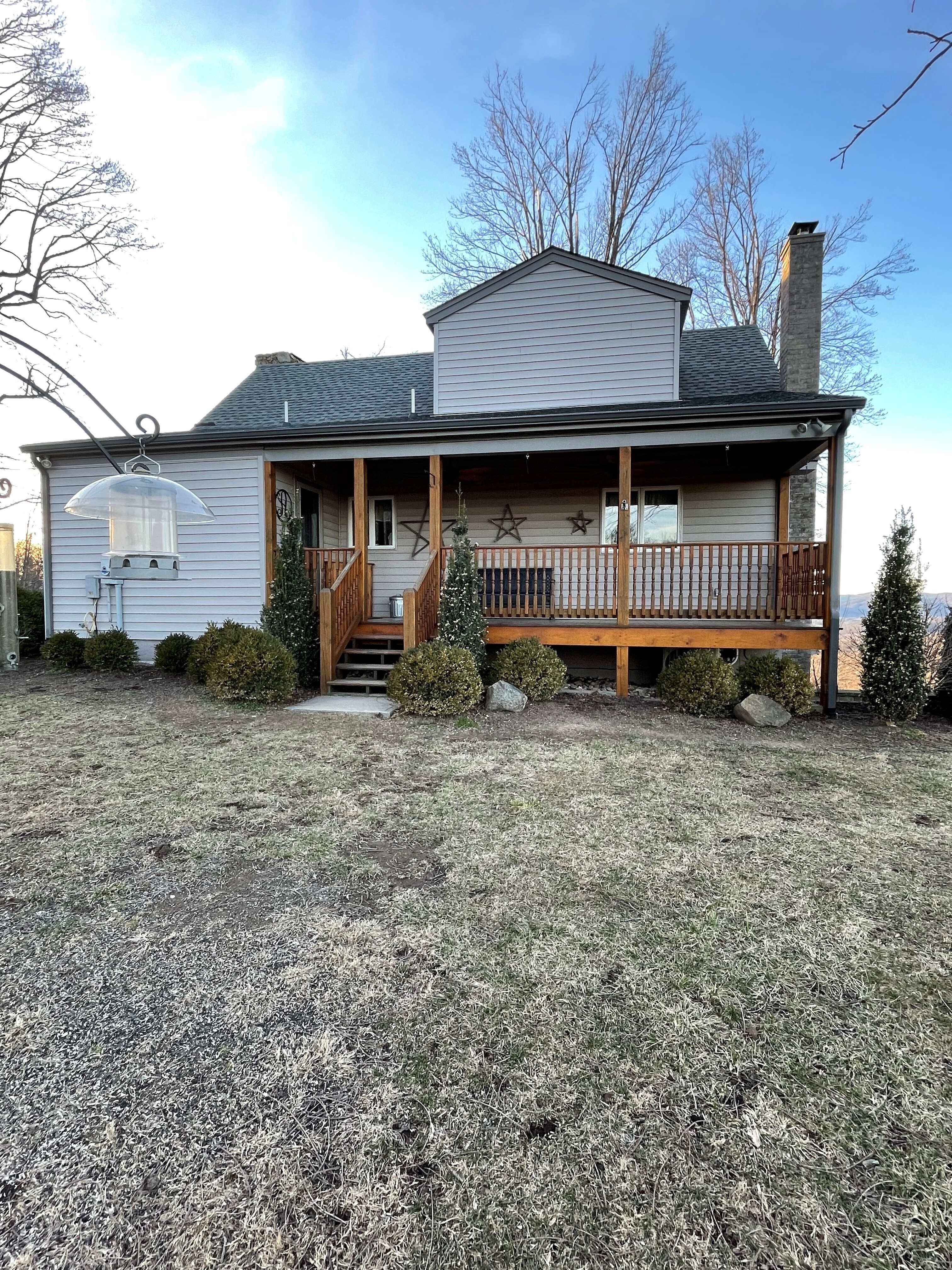 Back of cabin-style house with a covered front porch, wood railing, stone chimney, and a frosty yard in front under a clear sky belonging to Sponsored Residential Providers Jimmy and Nancy Ayers in Monroe, Virginia.