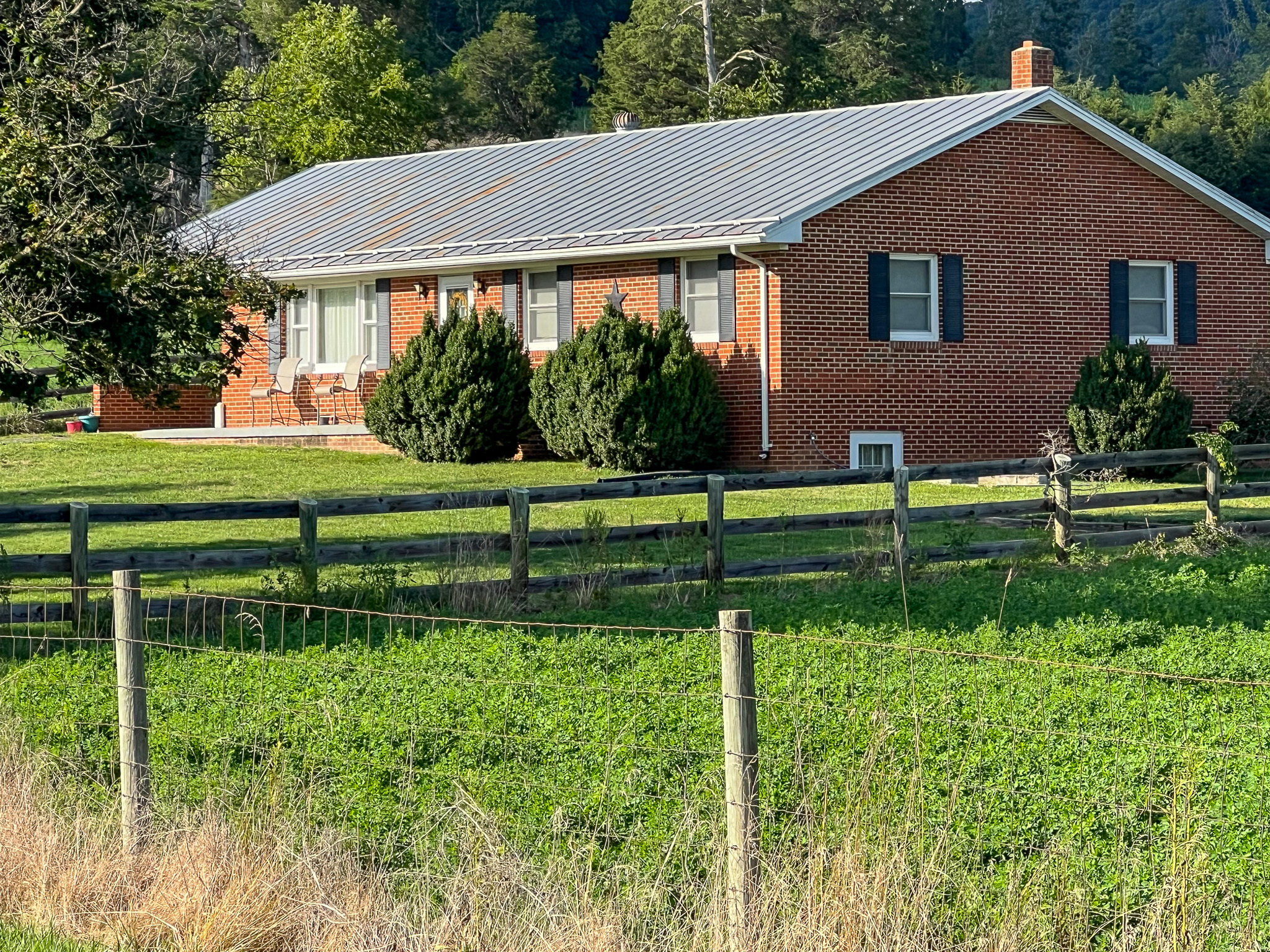 Brick ranch-style house with a gray roof, surrounded by green grass and fenced pasture on a sunny day belonging to Sponsored Residential Provider Rebecca Sherfey in Edinburg, Virginia.