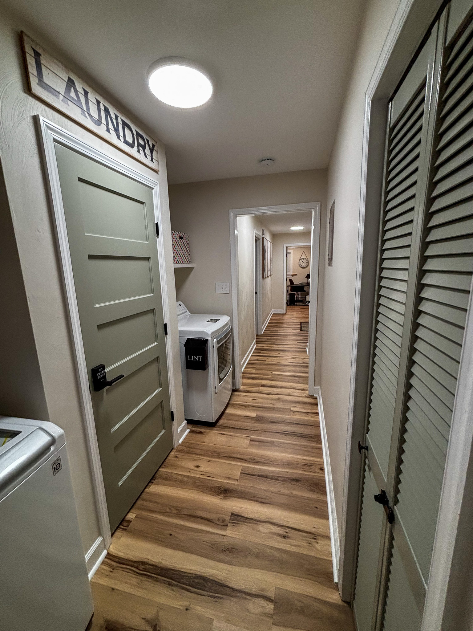 A hallway with wood floors, a laundry door, and a washer and dryer along the wall inside the home of sponsored residential provider Regina Hill in Roanoke, Virginia.