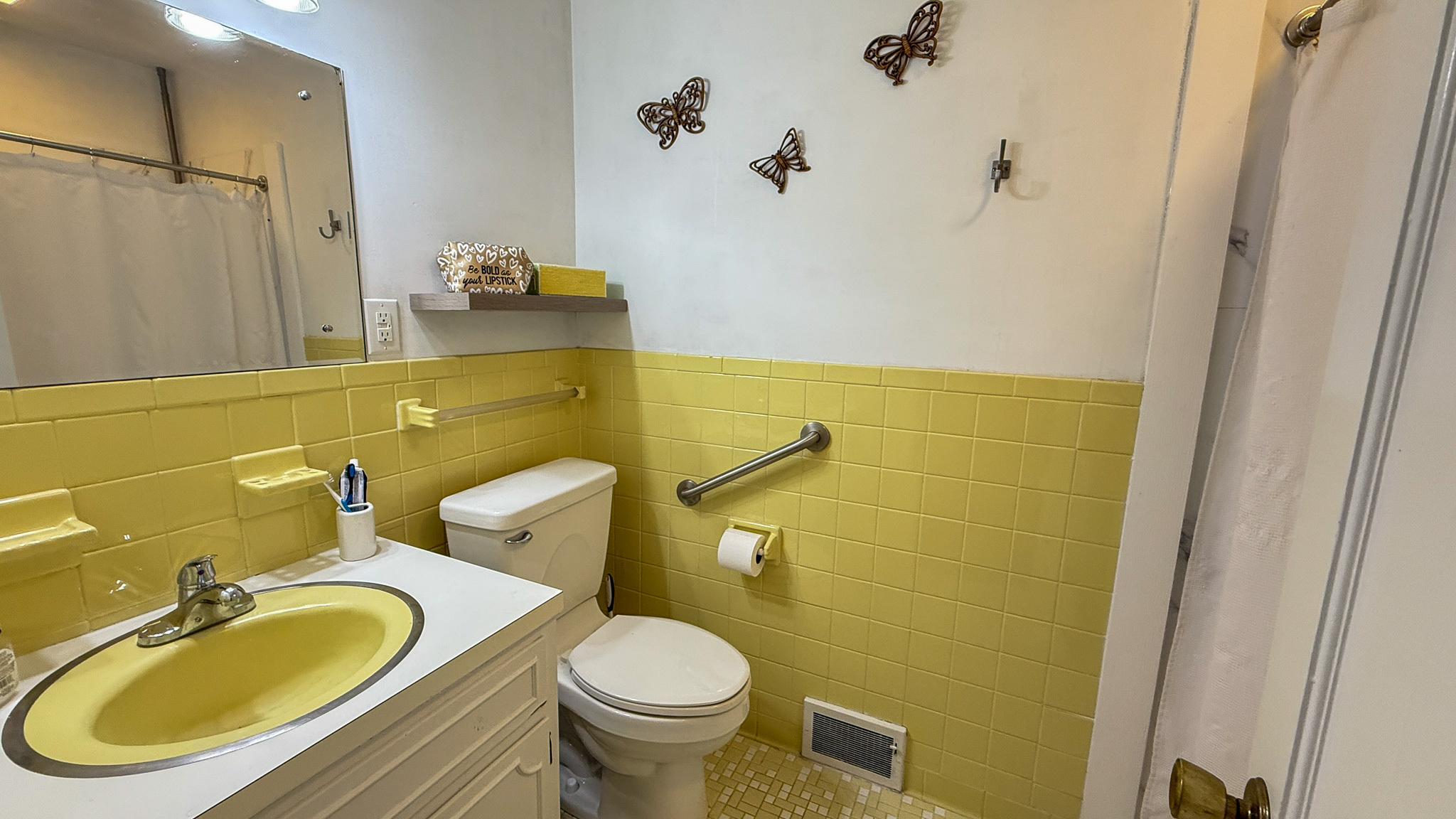 A small bathroom with yellow tile accents, a matching yellow sink, and a toilet beside a grab bar on the wall inside the home of Sponsored Residential Providers Angela and James Snyder in Rocky Mount, Virginia.