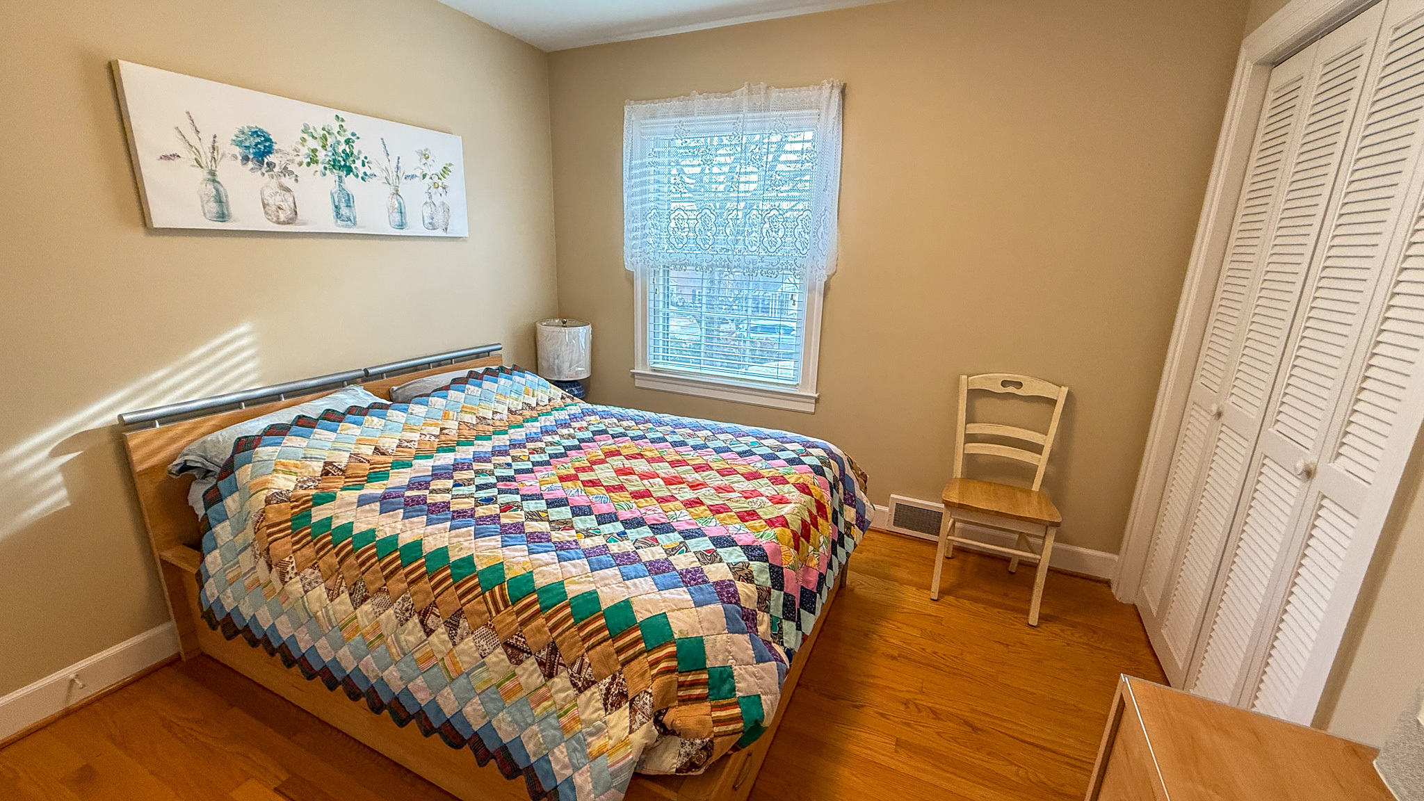 A bedroom with a colorful patchwork quilt on a wooden bed, a small nightstand, and a window centered on the back wall inside the home of Sponsored Residential Providers Angela and James Snyder in Rocky Mount, Virginia.