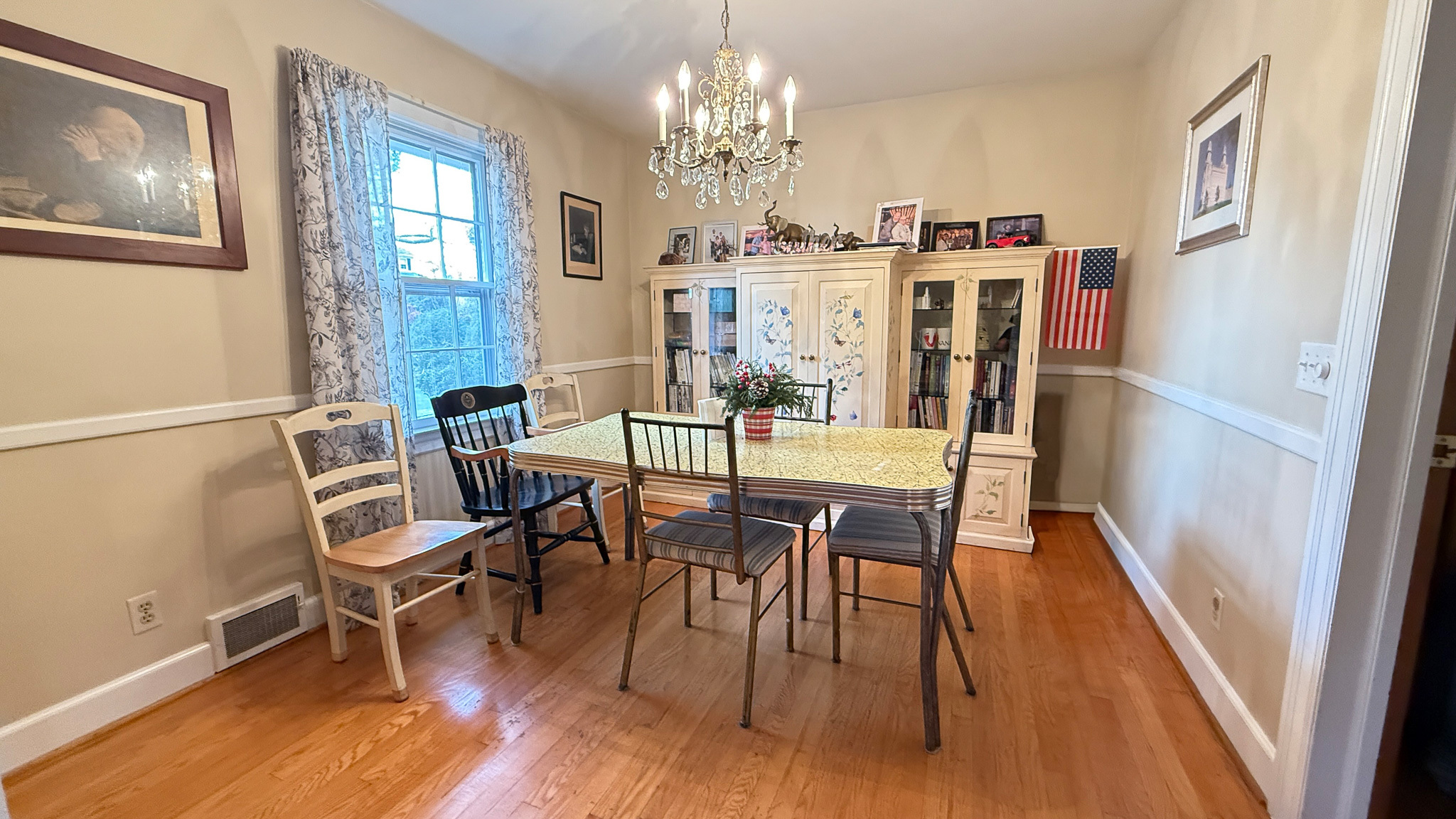 A dining room with a chandelier, mixed chairs around a rectangular table, and a large white cabinet displaying decor along the back wall inside the home of Sponsored Residential Providers Angela and James Snyder in Rocky Mount, Virginia.