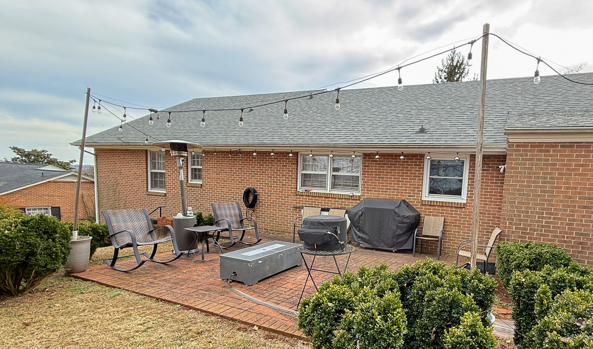 A brick patio with outdoor seating, string lights, and a grill arranged along the back of the house at  the home of Sponsored Residential Providers Angela and James Snyder in Rocky Mount, Virginia.