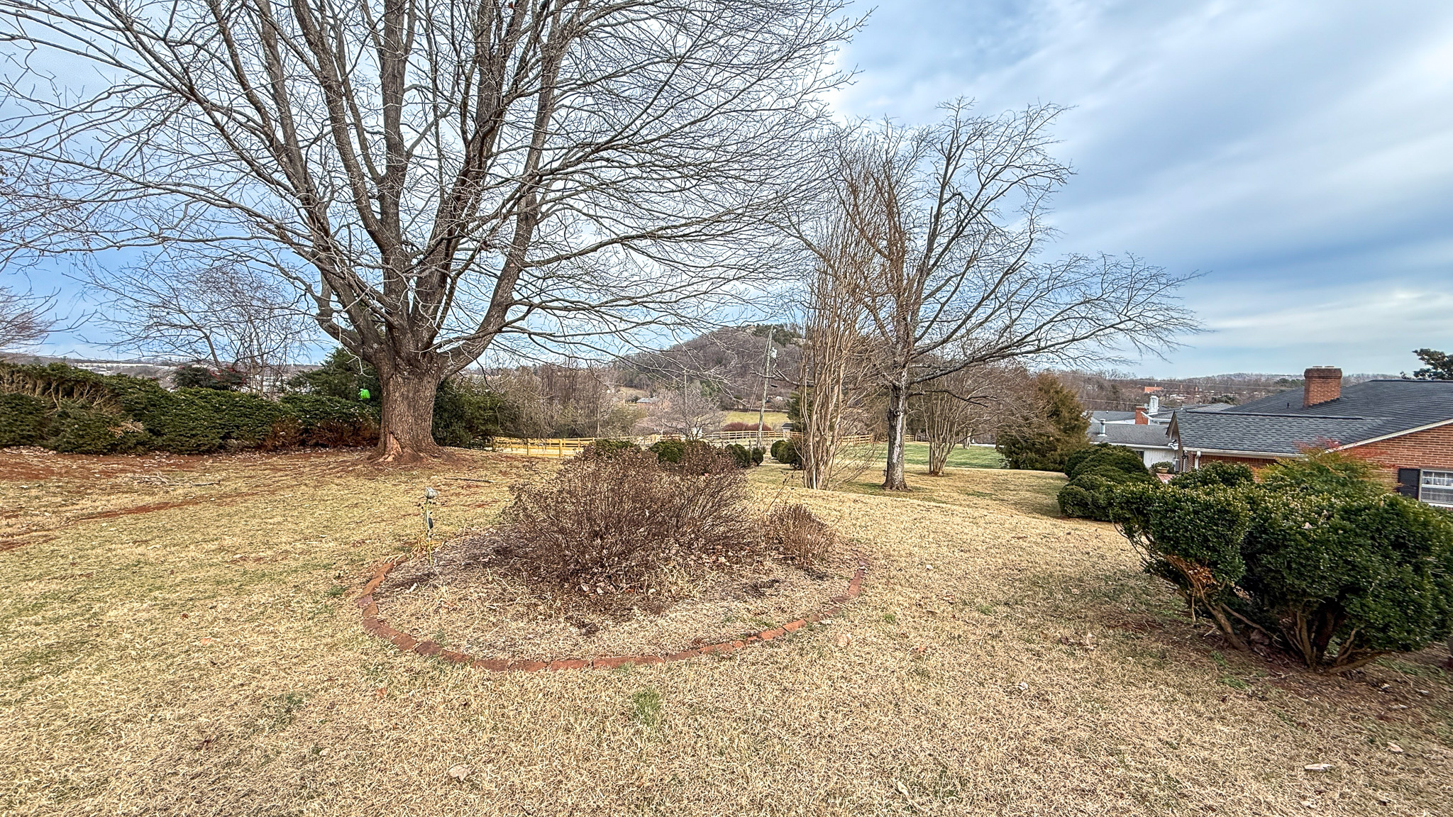 A large yard with mature trees, trimmed bushes, and a circular mulch bed in the foreground overlooking a sloping landscape at  the home of Sponsored Residential Providers Angela and James Snyder in Rocky Mount, Virginia.