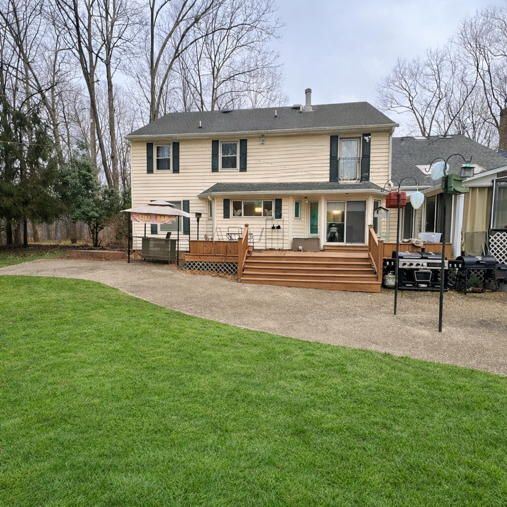 Wide backyard view of a two‑story beige house with a wooden deck, outdoor seating, and a grill, bordered by trees Sponsored Residential Provider Tarnisha Bradshaw in Fredericksburg, Virginia.
