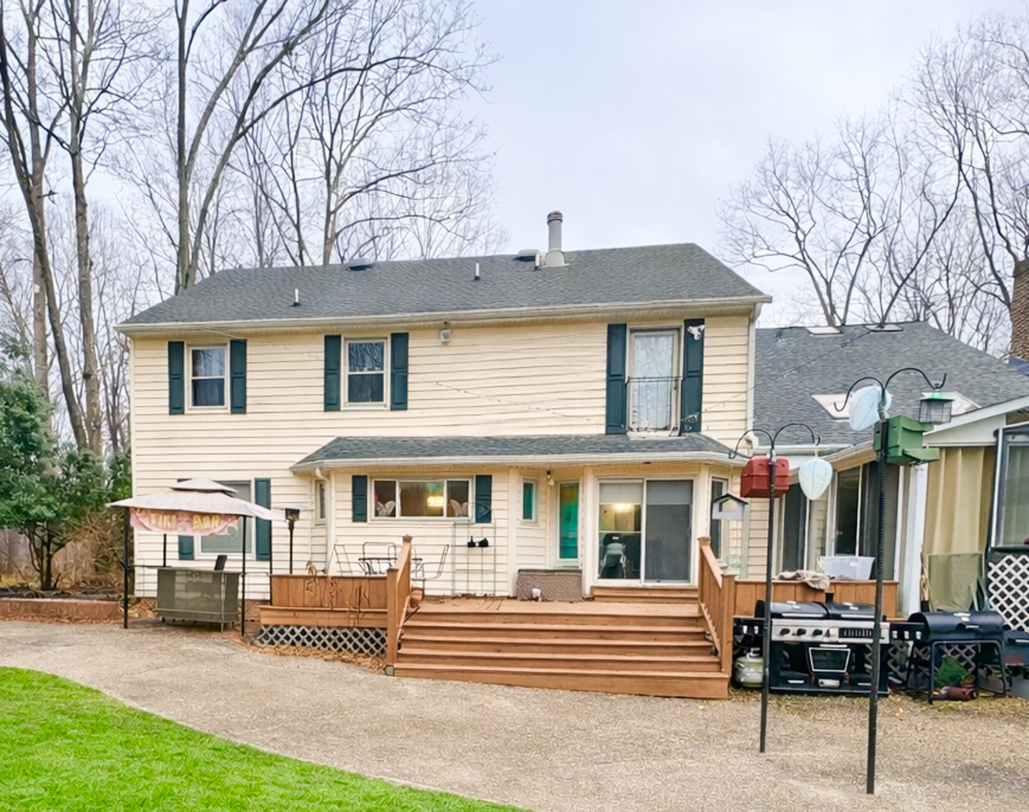 Back view of a two‑story beige house with a large wooden deck, outdoor seating, and a grill, surrounded by trees belonging to Sponsored Residential Provider Tarnisha Bradshaw in Fredericksburg, Virginia.