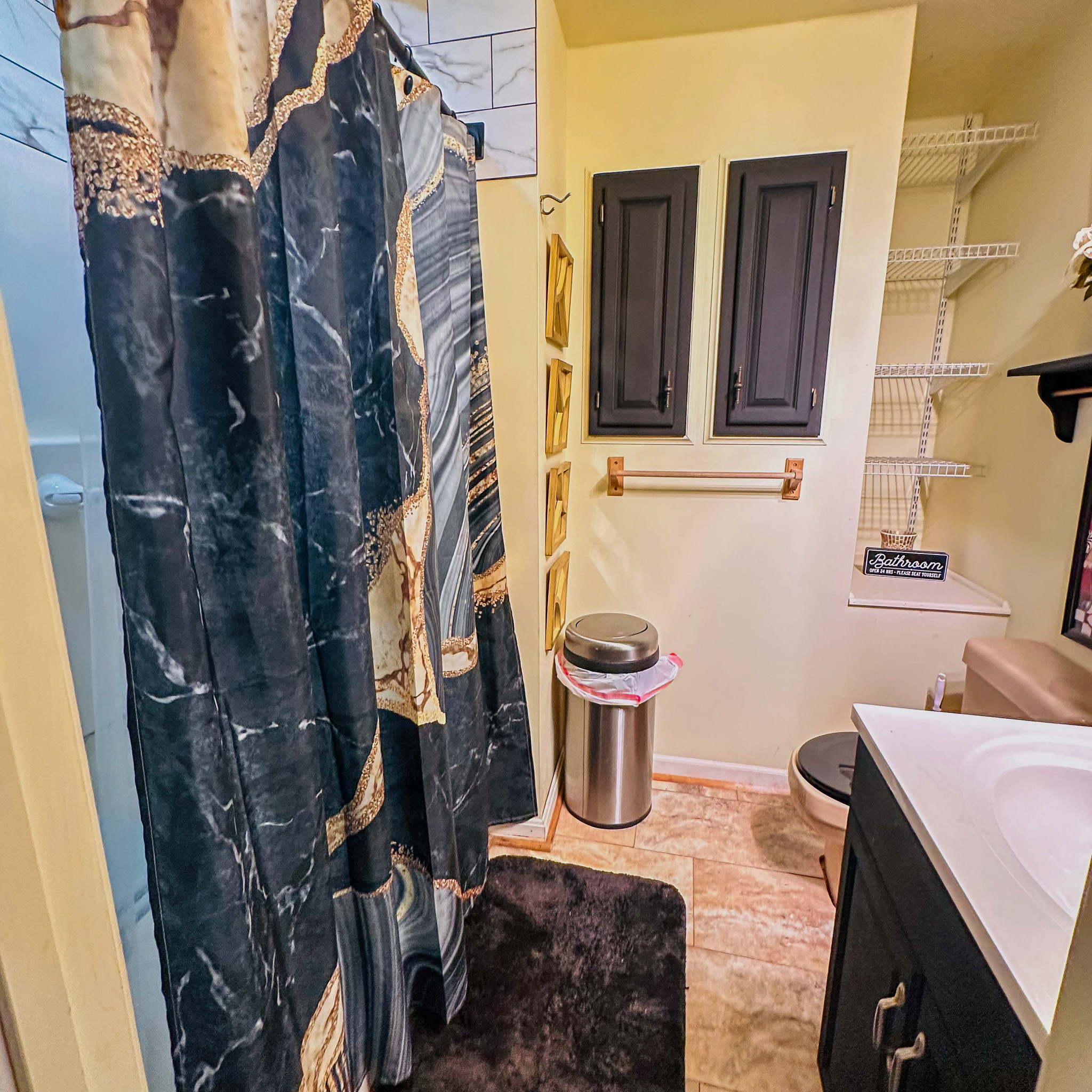 Small bathroom with a dark shower curtain, vanity with sink, toilet, and wall-mounted cabinets inside the home of Sponsored Residential Provider Tarnisha Bradshaw in Fredericksburg, Virginia.