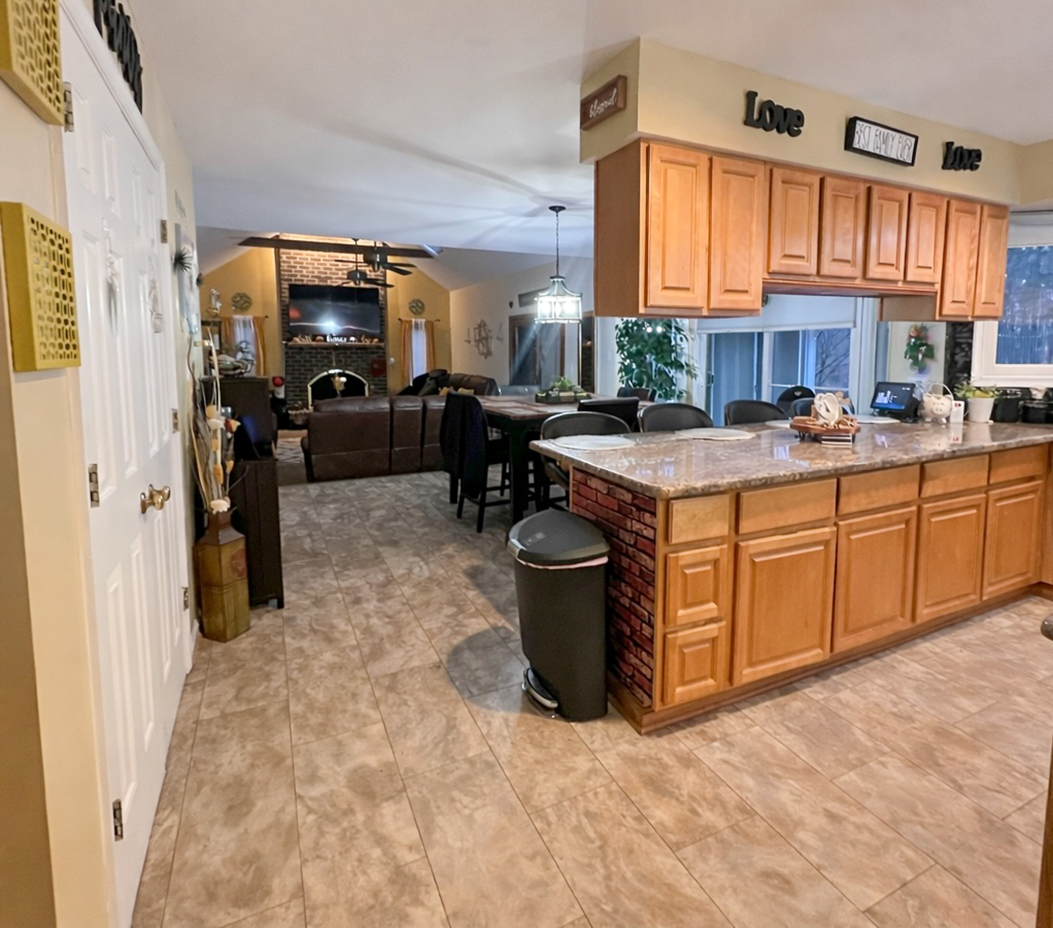 Open kitchen with wooden cabinets and large island overlooking a living room with sofas, fireplace, and TV inside the home of Sponsored Residential Provider Tarnisha Bradshaw in Fredericksburg, Virginia.