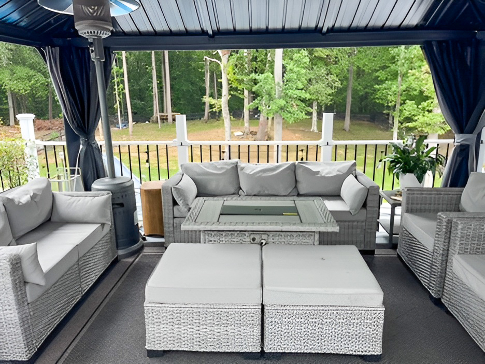 Covered patio with light gray wicker furniture and cushioned seating, overlooking a wooded backyard outside the home of Group Home Providers Alex and Dillon Tittle in Fredericksburg, Virginia.