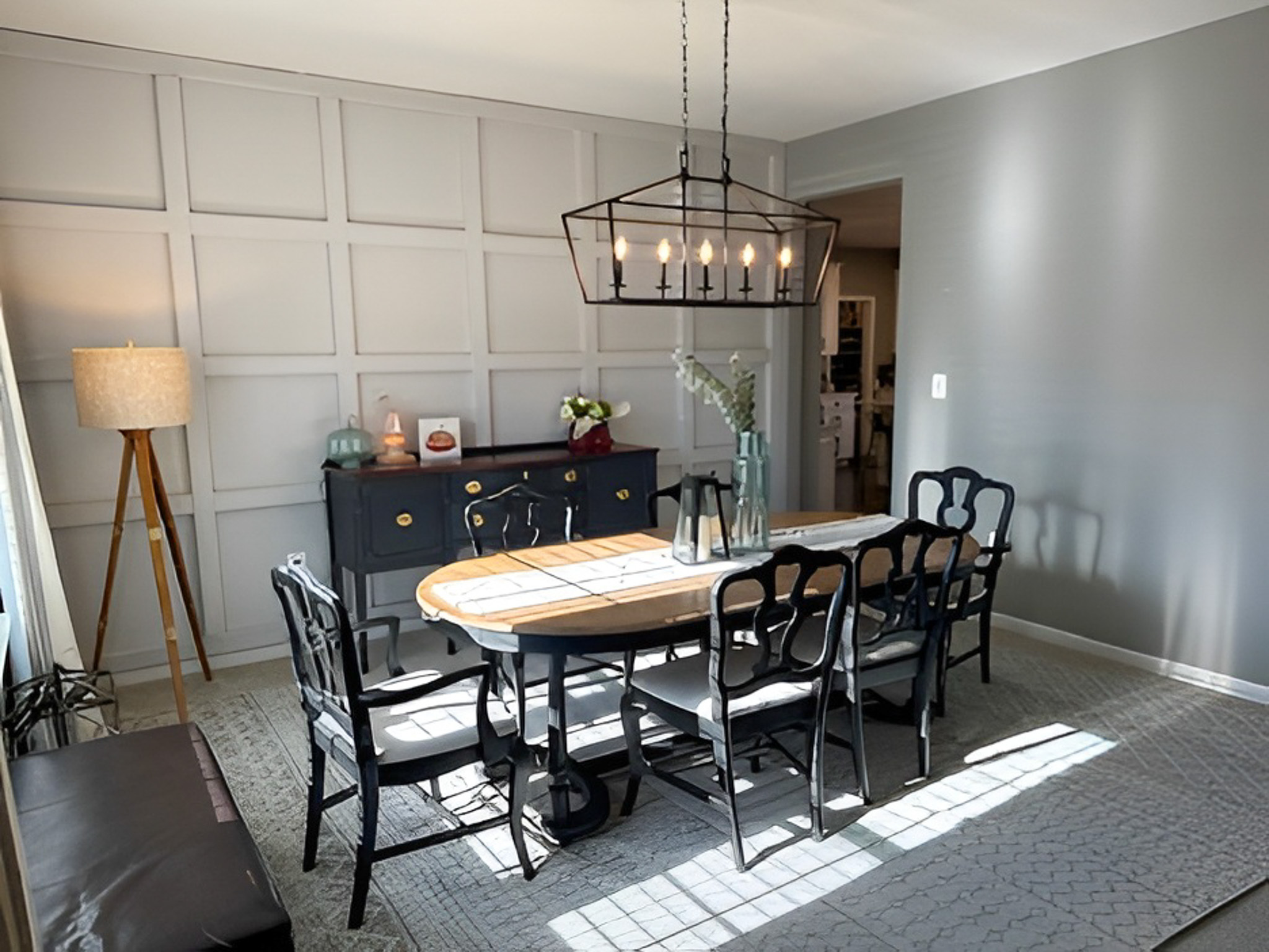Bright dining room with an oval table, black chairs, a modern chandelier, and a paneled accent wall with a sideboard inside the home of Group Home Providers Alex and Dillon Tittle in Fredericksburg, Virginia.