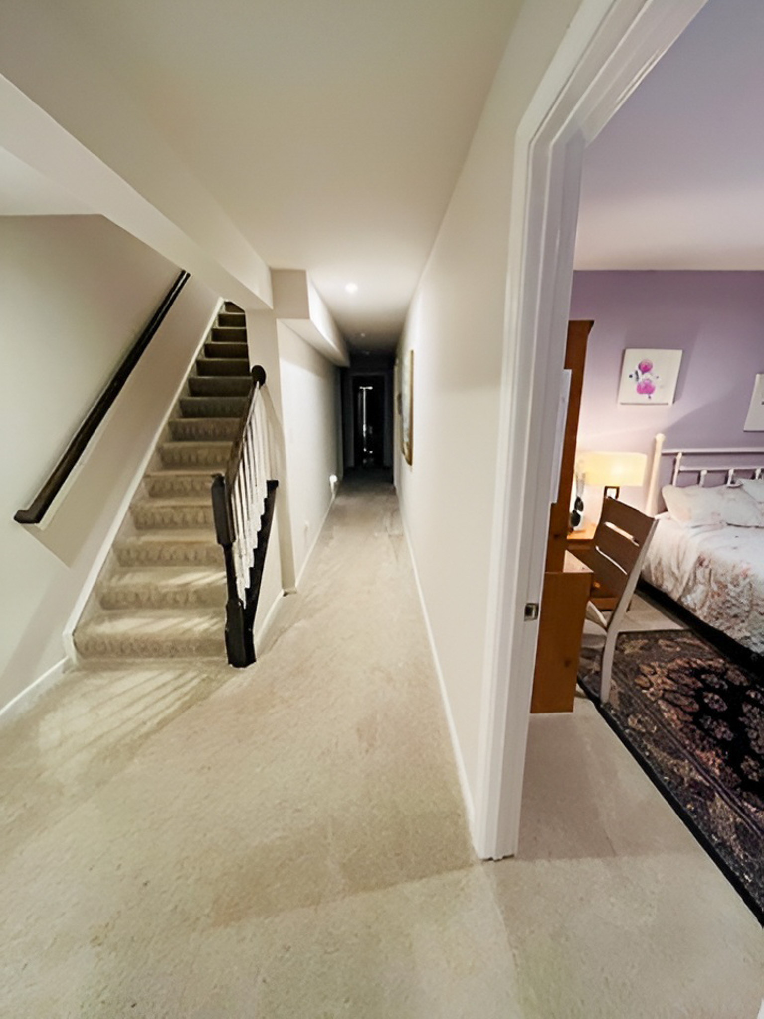 Hallway with carpeted stairs on the left and a bedroom with lavender walls visible on the right inside the home of Group Home Providers Alex and Dillon Tittle in Fredericksburg, Virginia.