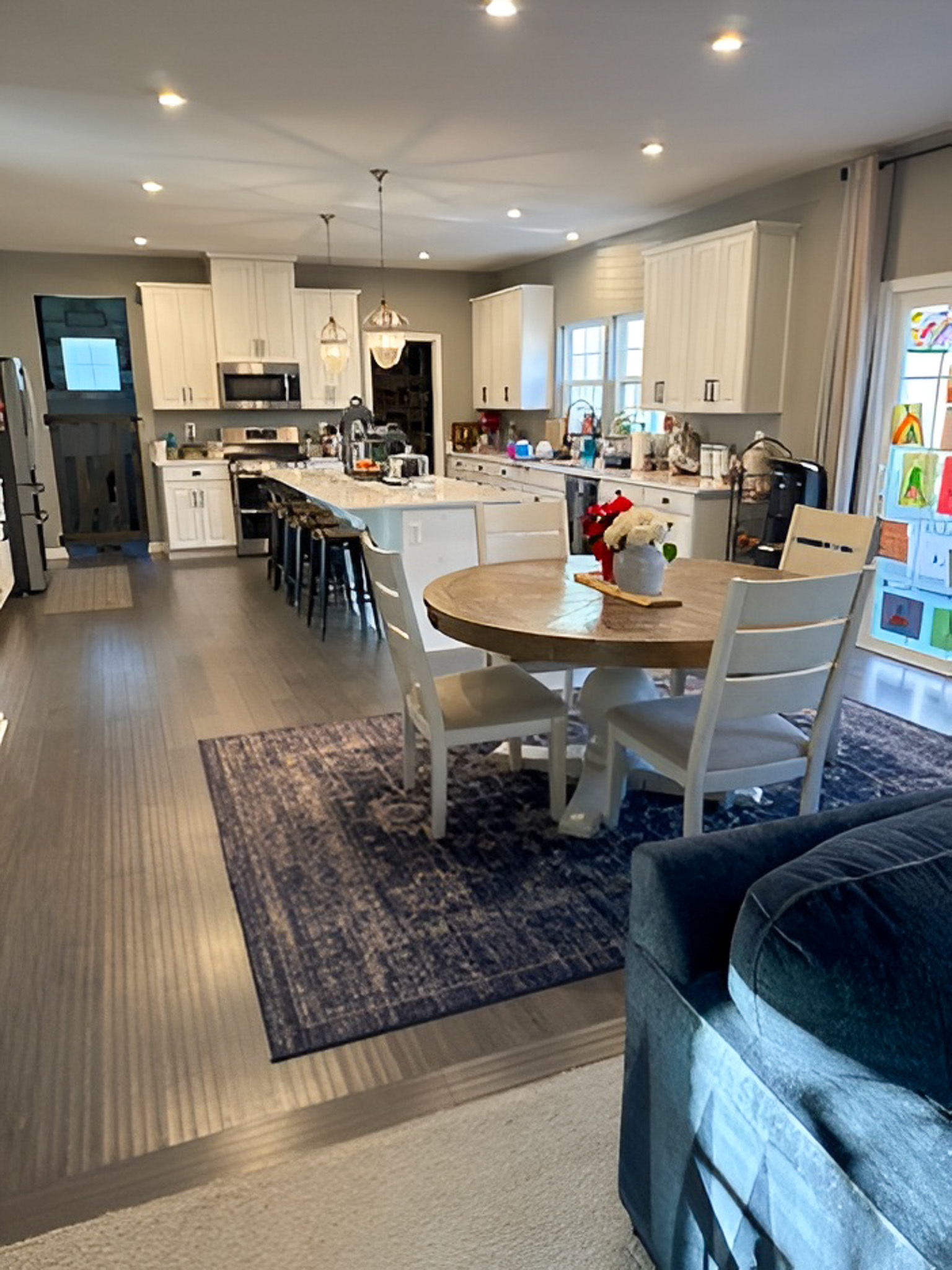Open kitchen and dining area with white cabinets, a large island with barstools, a round dining table, and dark wood flooring inside the home of Group Home Providers Alex and Dillon Tittle in Fredericksburg, Virginia.
