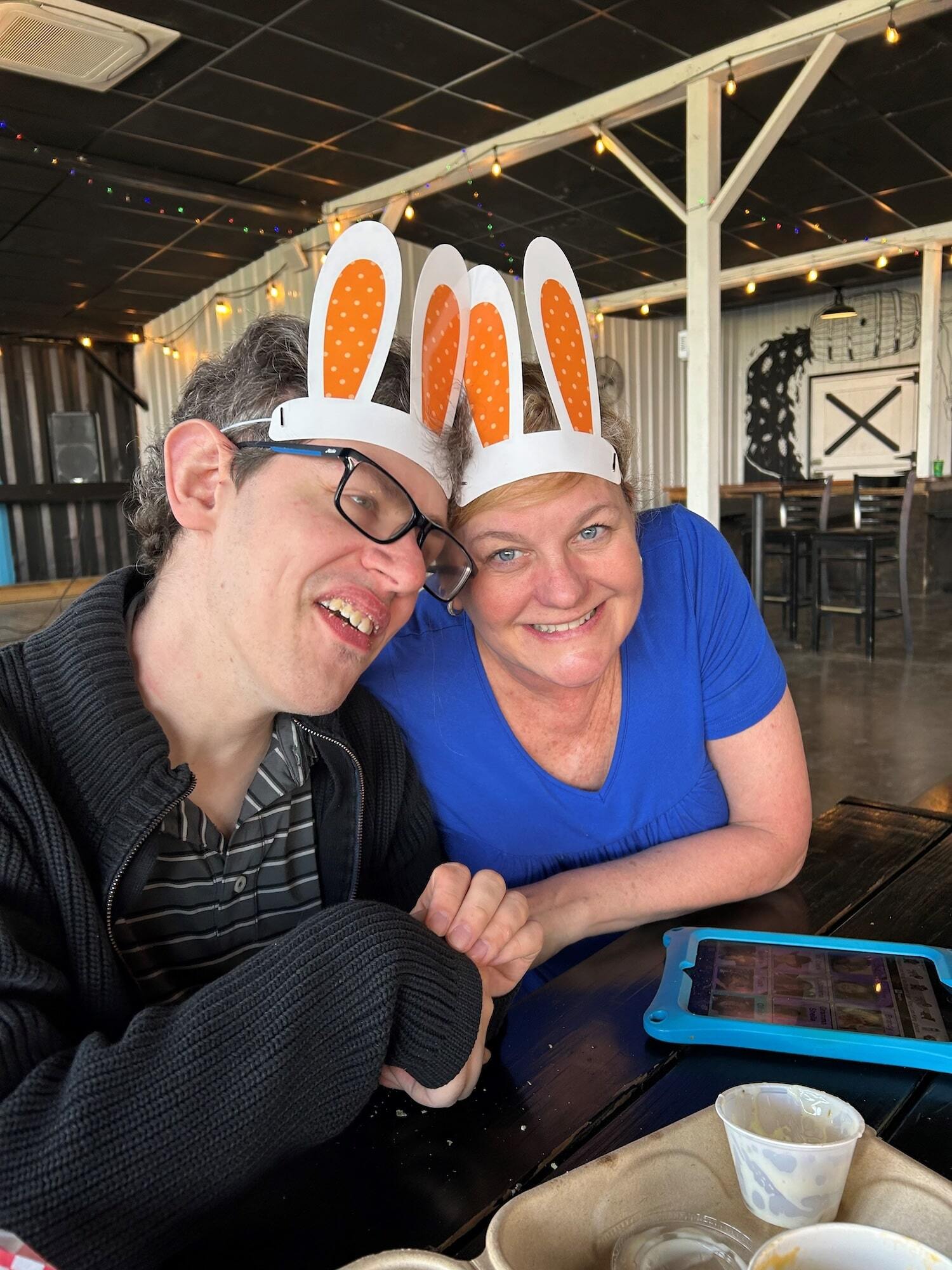 A man and woman wearing bunny ear decorations on their heads holding hands while sitting at a table