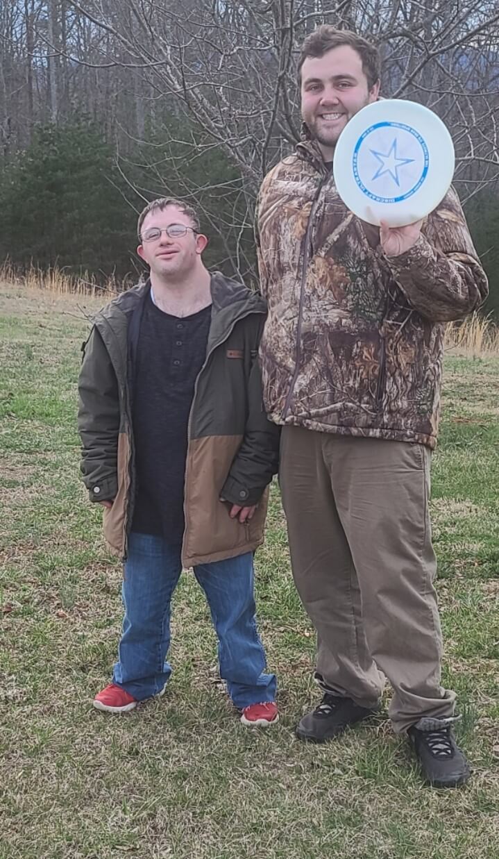 Two men standing outside smiling and holding a frisbee
