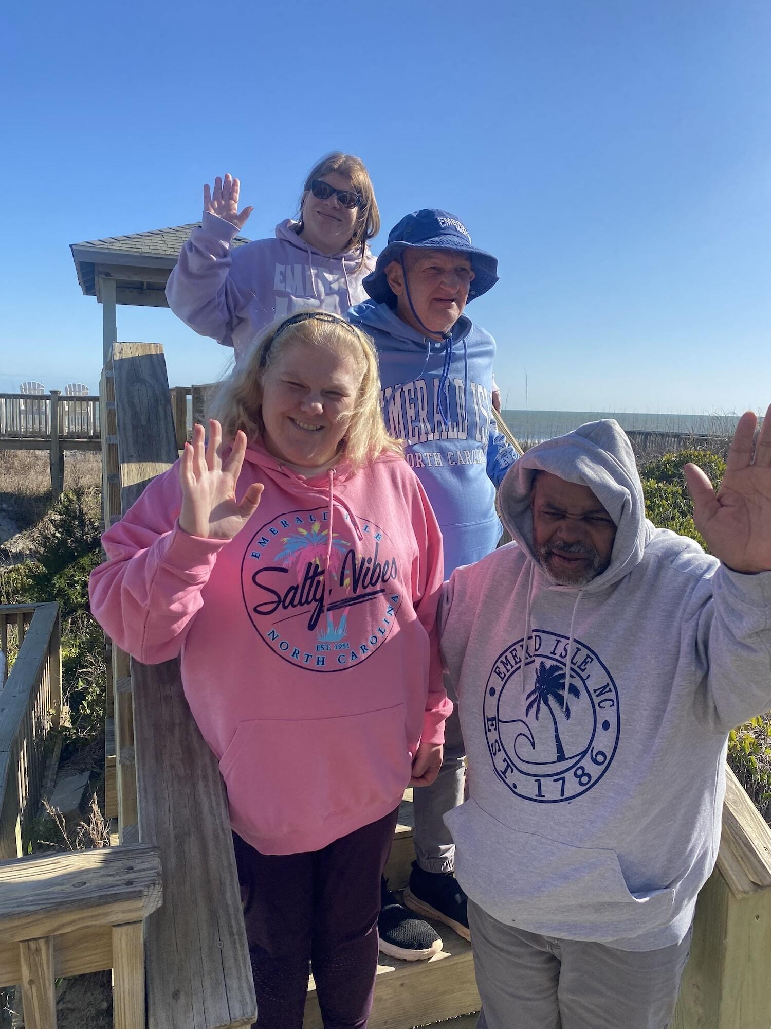 Four individuals waving at the camera on vacation at the beach