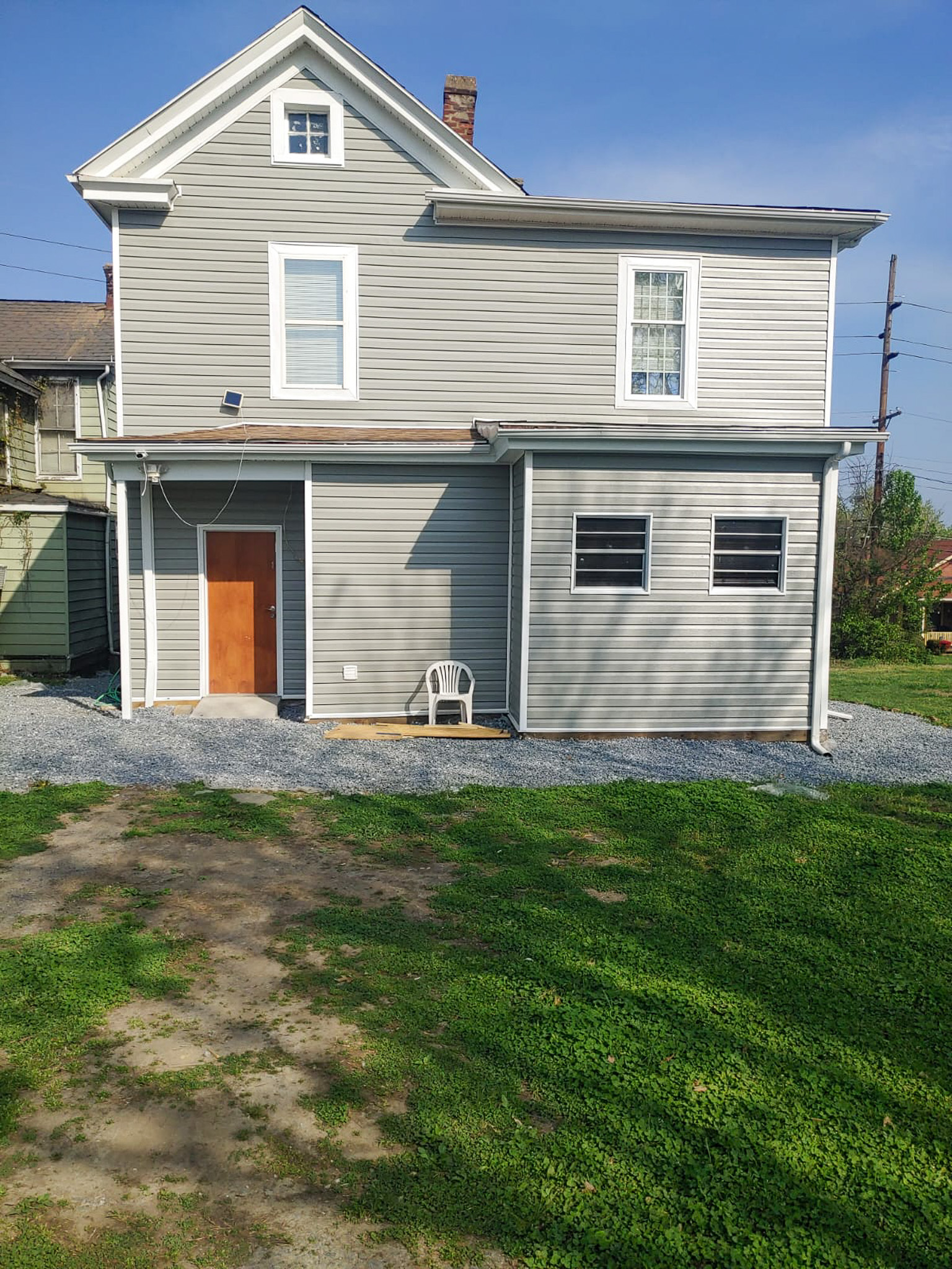 Rear view of a gray two‑story house with a brown door, several windows, and a gravel walkway beside a grassy yard belonging to Sponsored Residential Providers Gladys and Victor Oluwaji in Lynchburg, Virginia.
