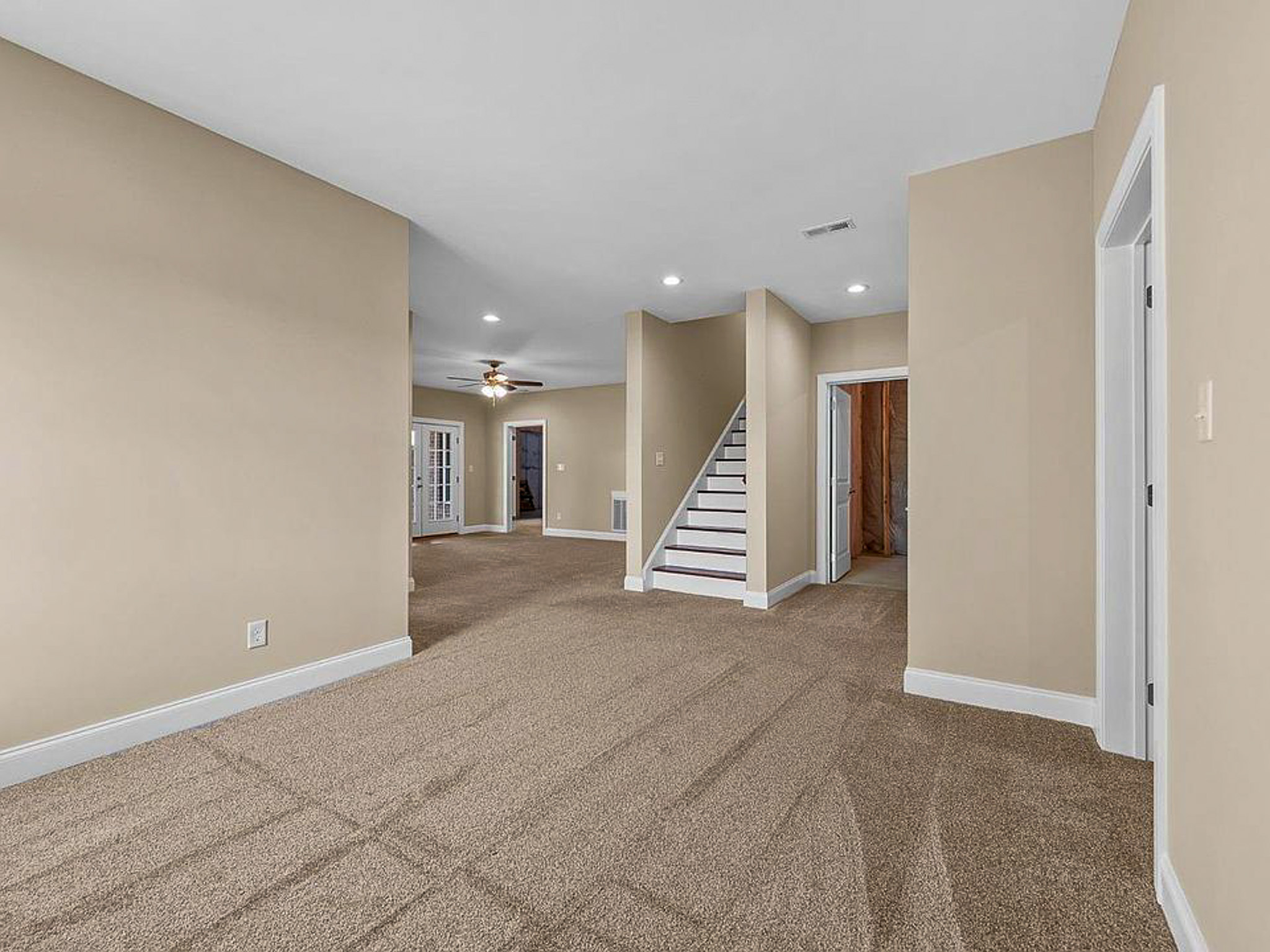 Carpeted lower‑level space with neutral walls, recessed lighting, and a staircase leading upward in the home of sponsored residential provider Lisa Reed in Lynchburg, Virginia