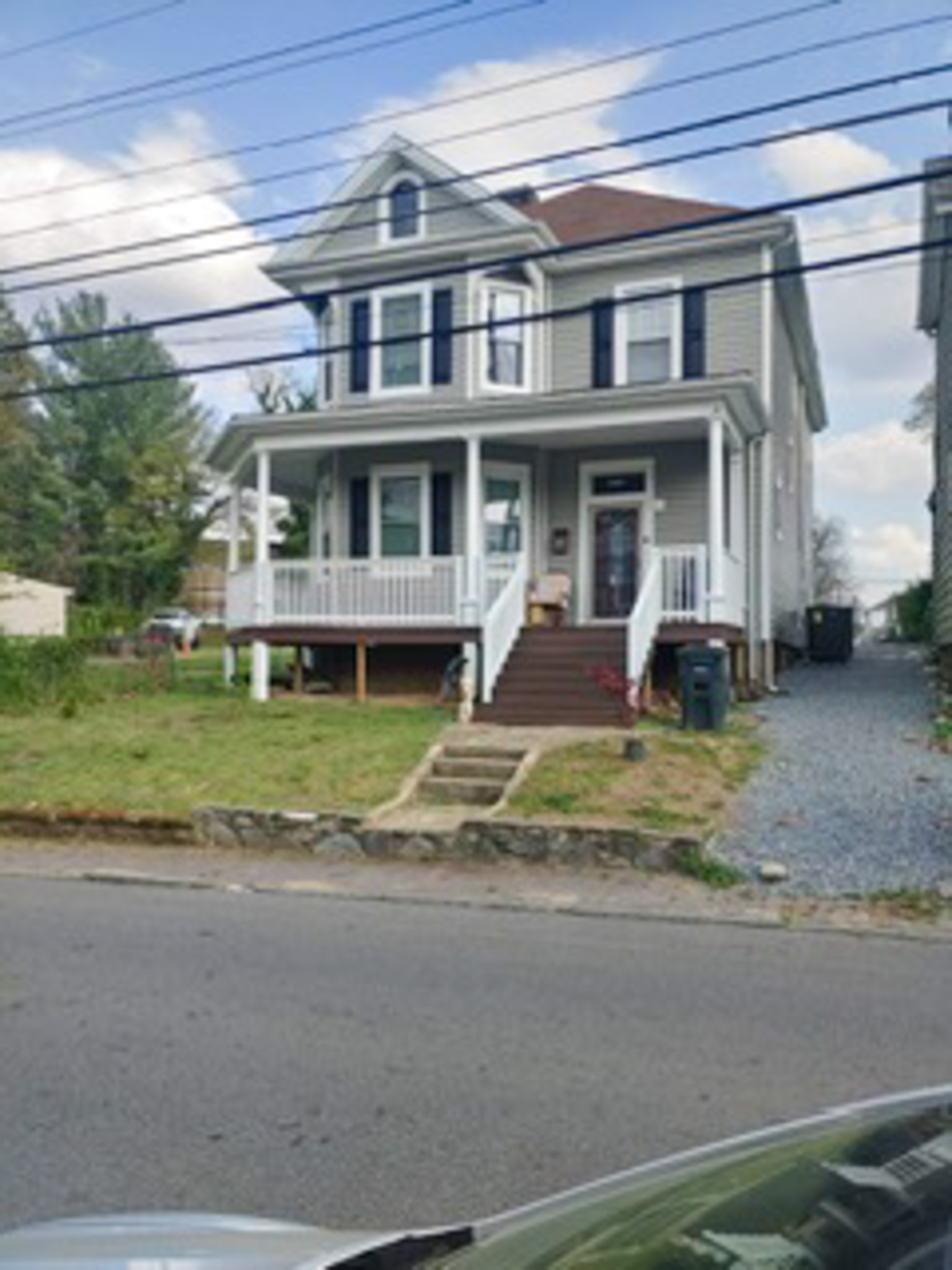 Two‑story gray house with a front porch, dark shutters, and steps leading up from the street, with a gravel driveway on the right side belonging to Sponsored Residential Providers Gladys and Victor Oluwaji in Lynchburg, Virginia.
