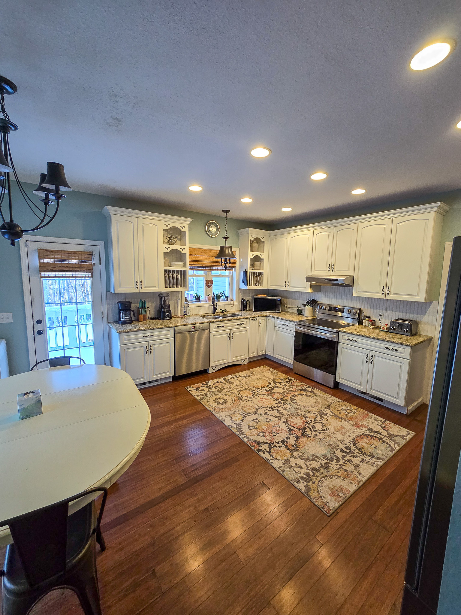 A spacious kitchen with white cabinets, stainless‑steel appliances, recessed lighting, hardwood floors, a patterned rug, and a small round dining nook to the left inside the home of Sponsored Residential Provider Chris Sumner in Galax, Virginia.