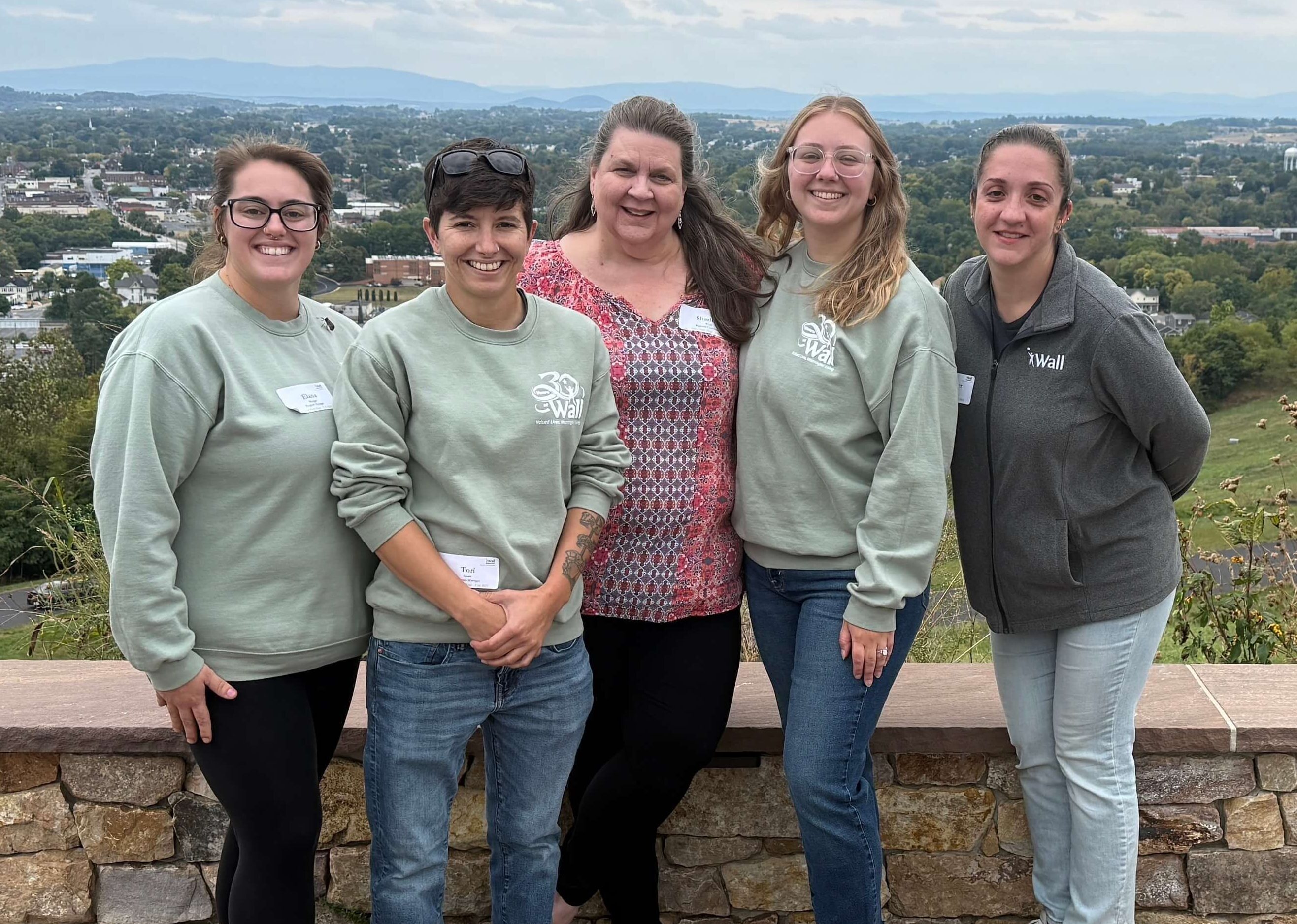 A group of five women employees of Wall wearing logo apparel in front of a scenic overlook.