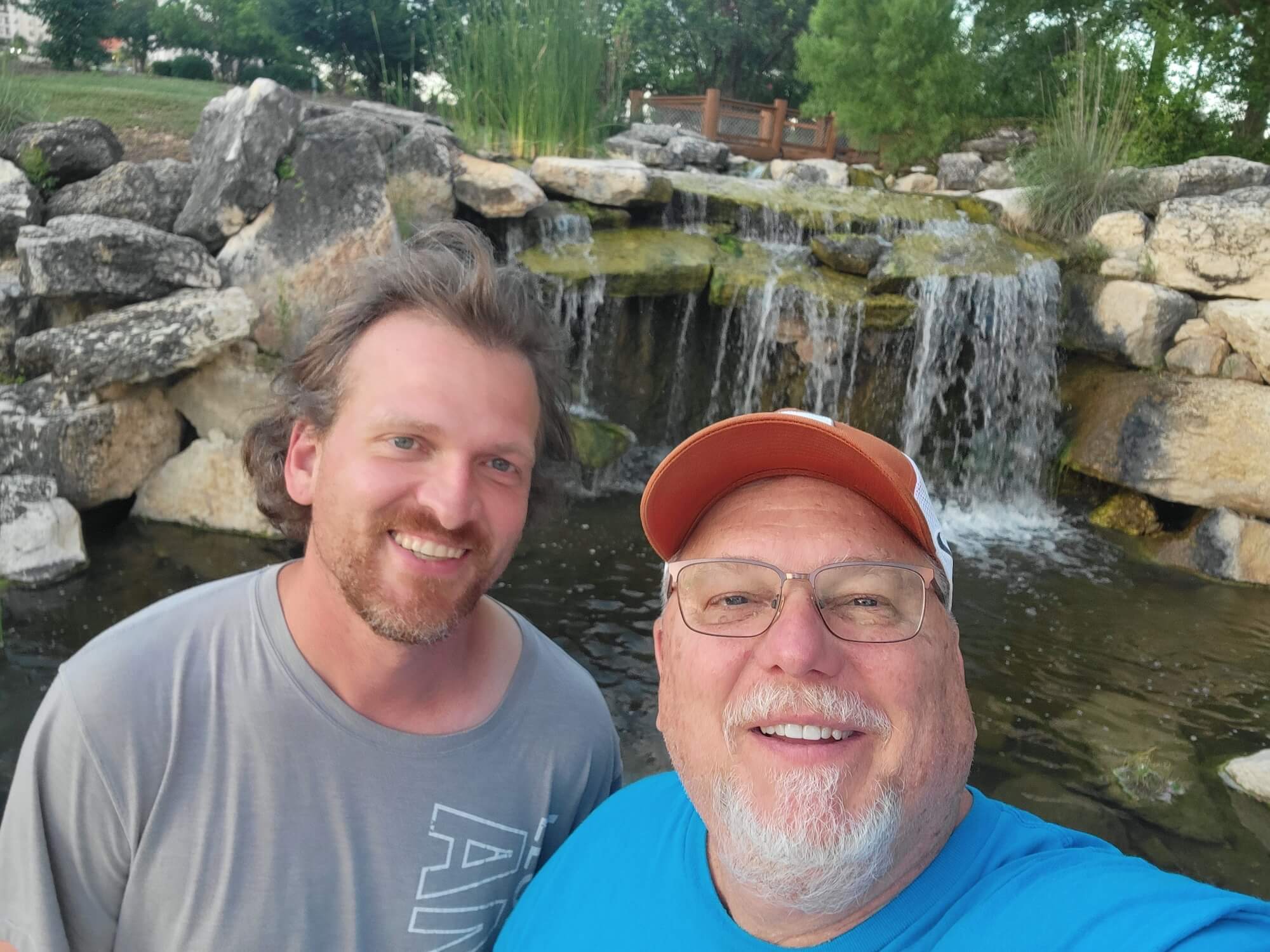 Two men smiling at camera in front of a waterfall
