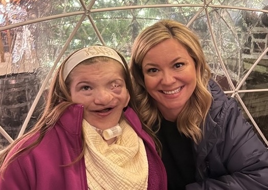 Two women smiling in front of an igloo decorated for the holidays
