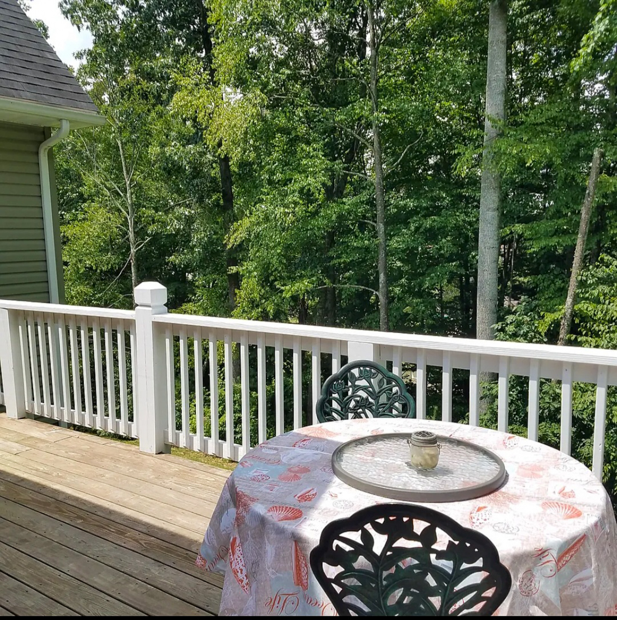 A wooden deck with a round table covered by a patterned cloth and metal chairs, overlooking a wooded area behind a white railing at the home of Sponsored Residential Provider Chris Sumner in Galax, Virginia.
