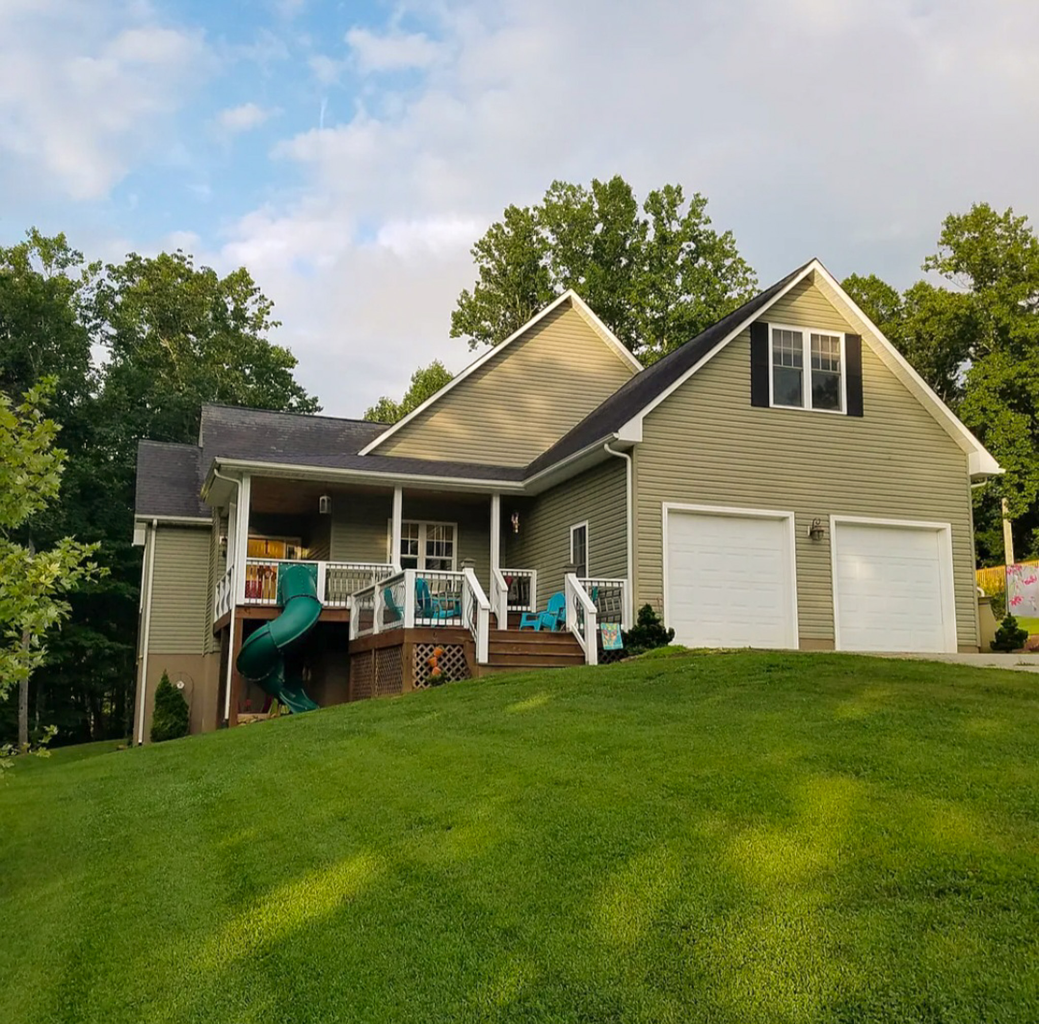 A tan two‑story house with a porch, two white garage doors, a slide on the side, and a well‑kept green lawn surrounded by trees belonging to Sponsored Residential Provider Chris Sumner in Galax, Virginia.