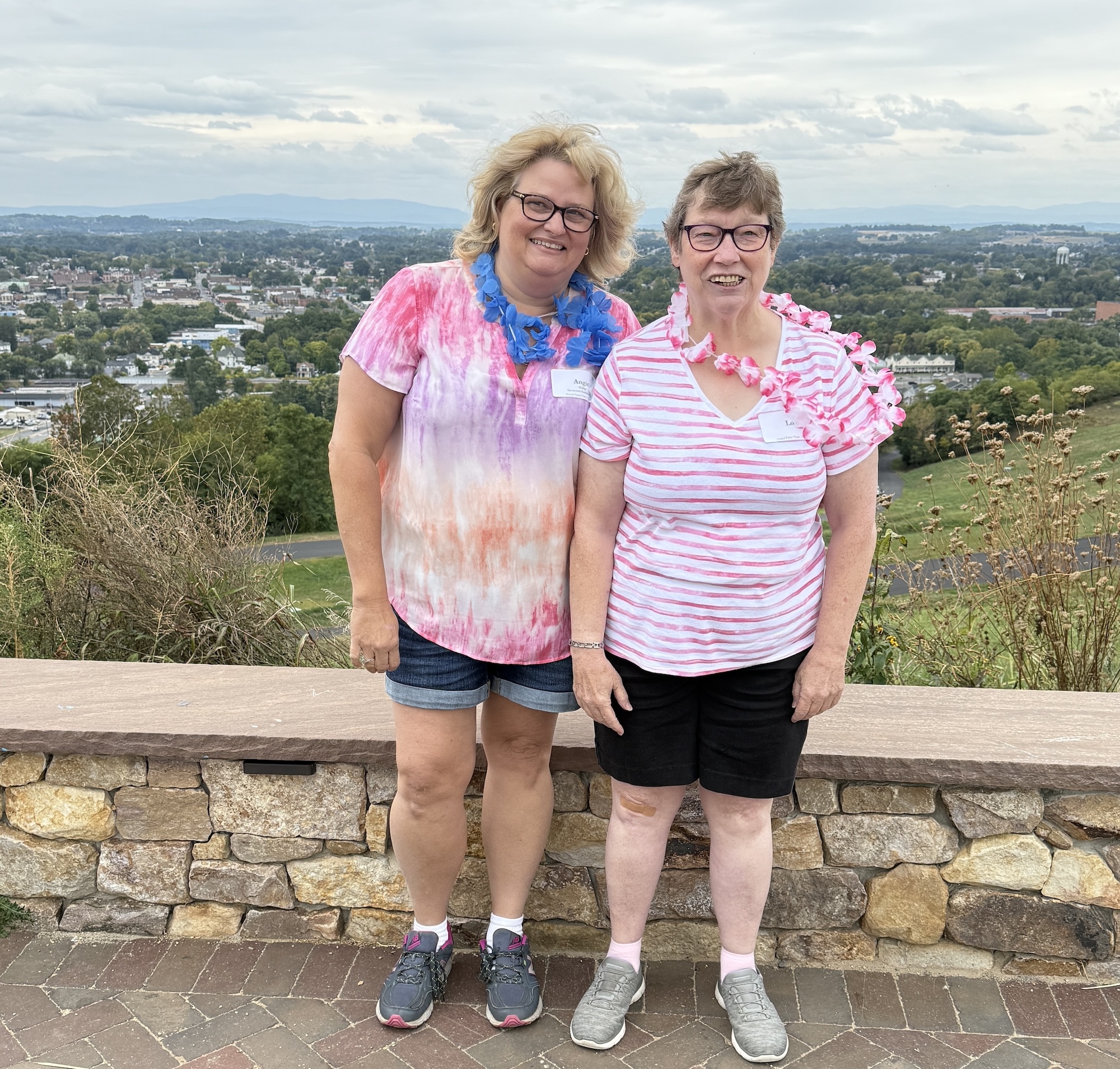 Two women standing in front of a scenic overlook wearing flowers leis