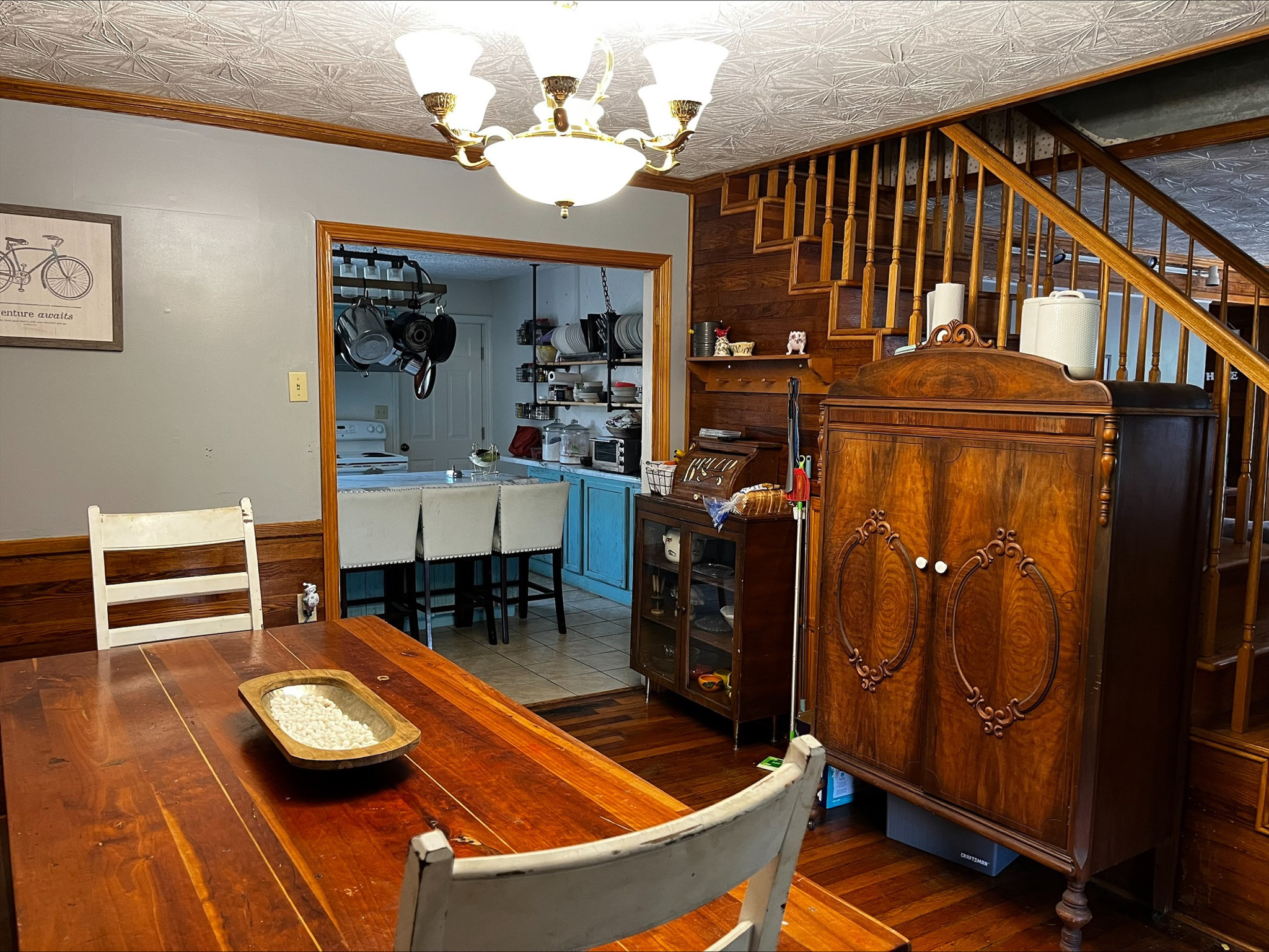 Dining room with a wooden table and chairs, antique cabinet, and a view into a kitchen with blue cabinetry beyond inside the home of Sponsored Residential Provider Dara Short in Willis, Virginia.