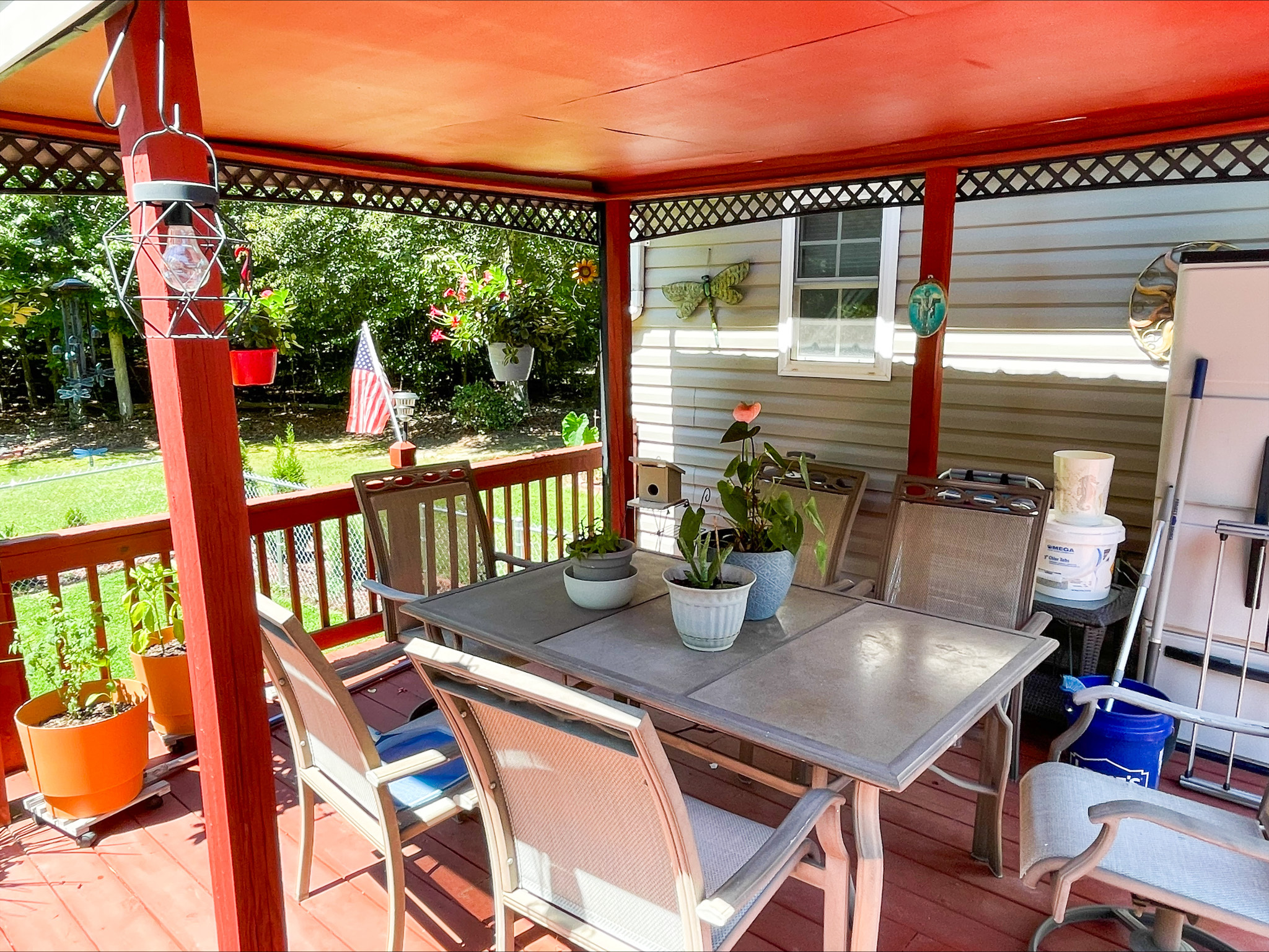 Covered backyard deck with a patio table and chairs, potted plants, and red-painted posts overlooking a grassy yard outside the home of Sponsored Residential Provider Kellie Lynch in Gloucester, Virginia.
