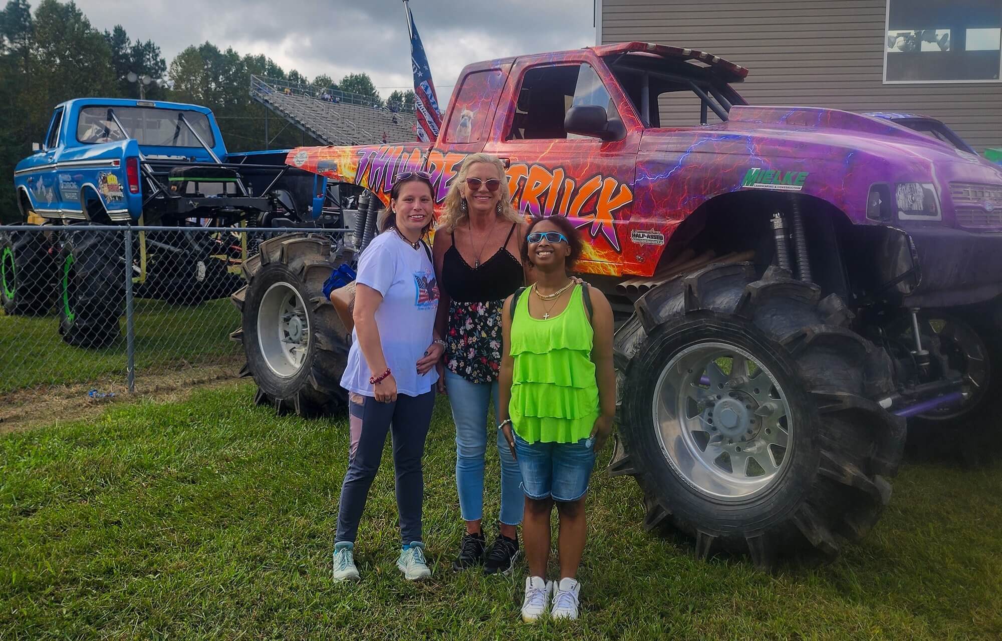 Three women pose in front of a purple and orange monster truck