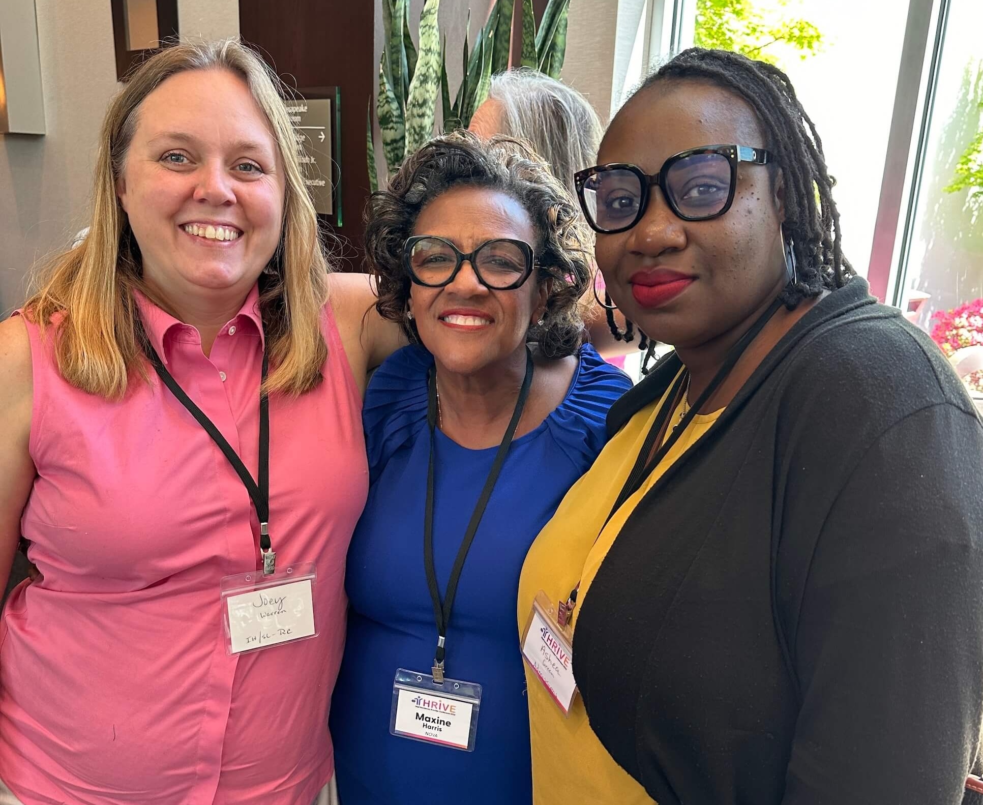 Three women wearing lanyard name tags at a conference smiling