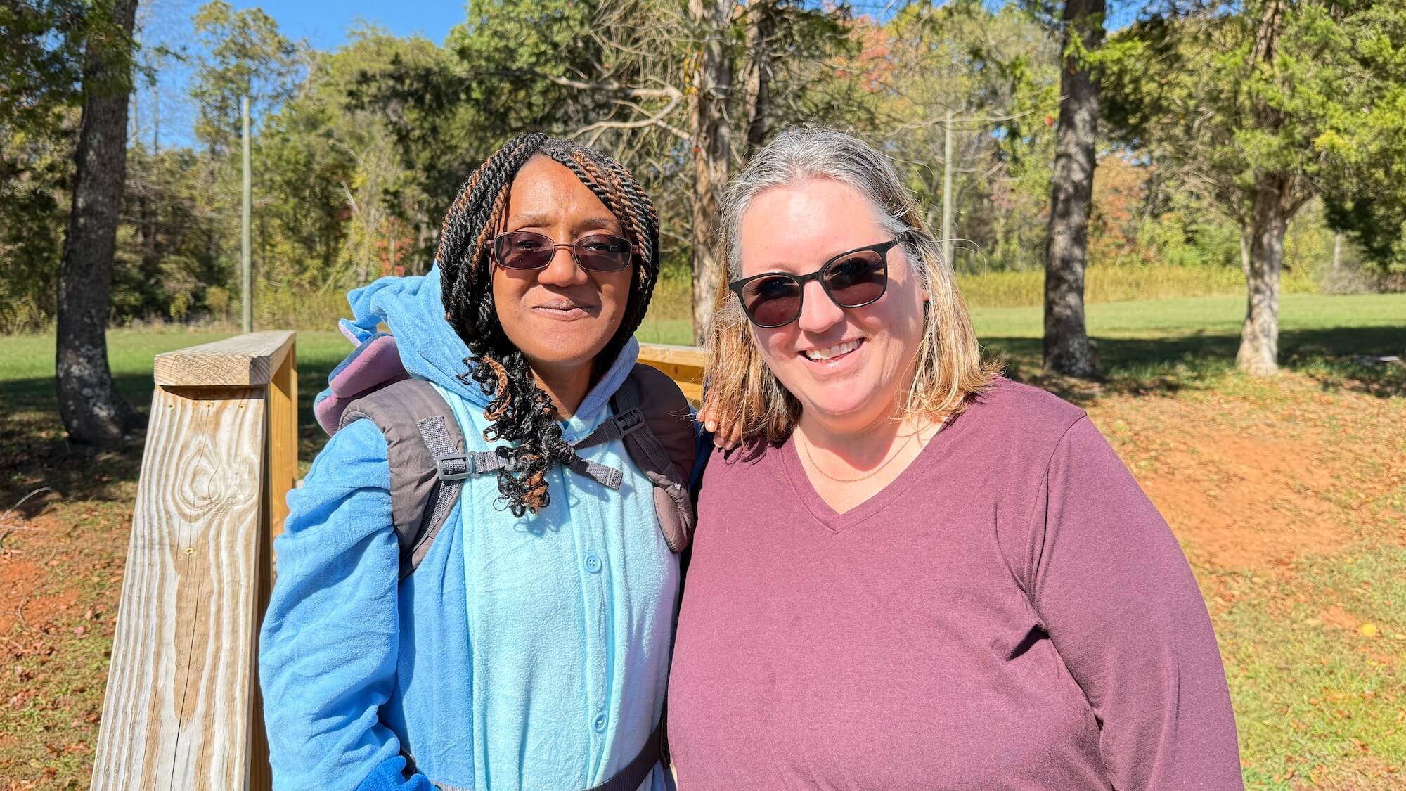 Two women standing outside wearing sunglasses smiling at the camera