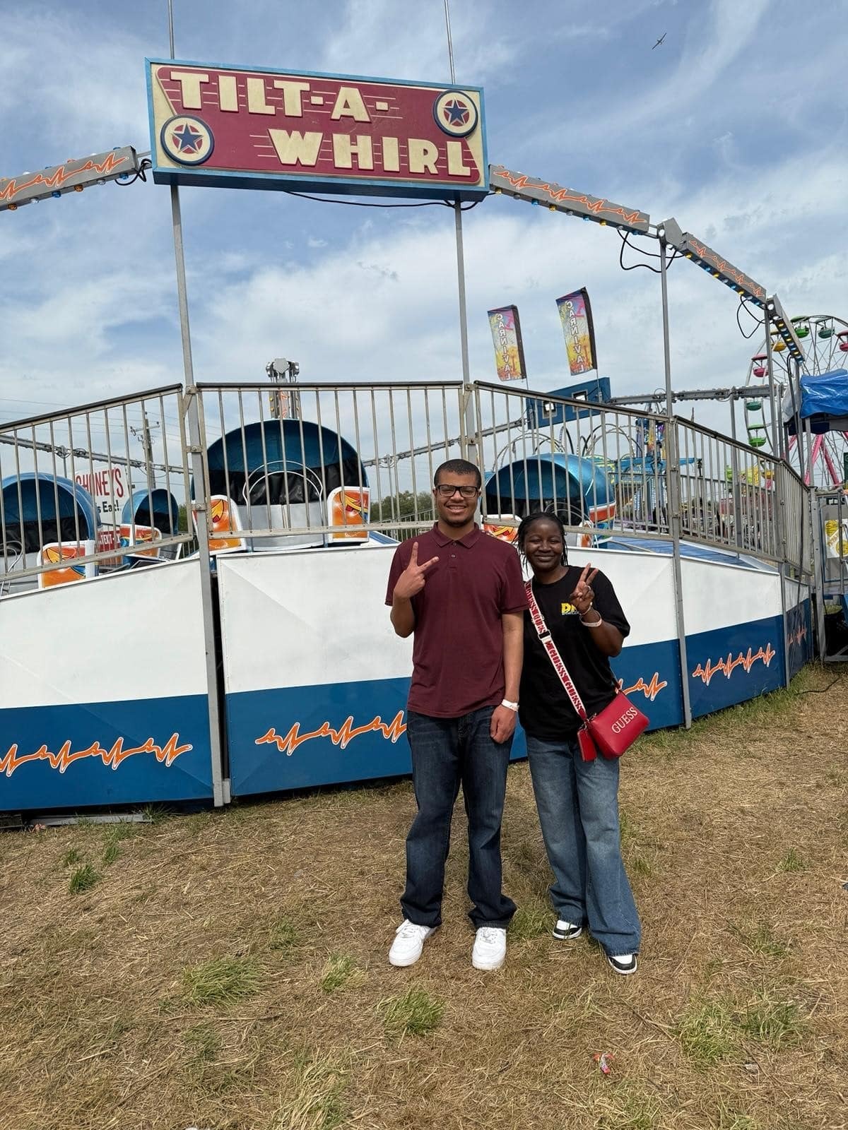 A man and woman holding up peace signs with their hands in front of a tilt-a-whirl